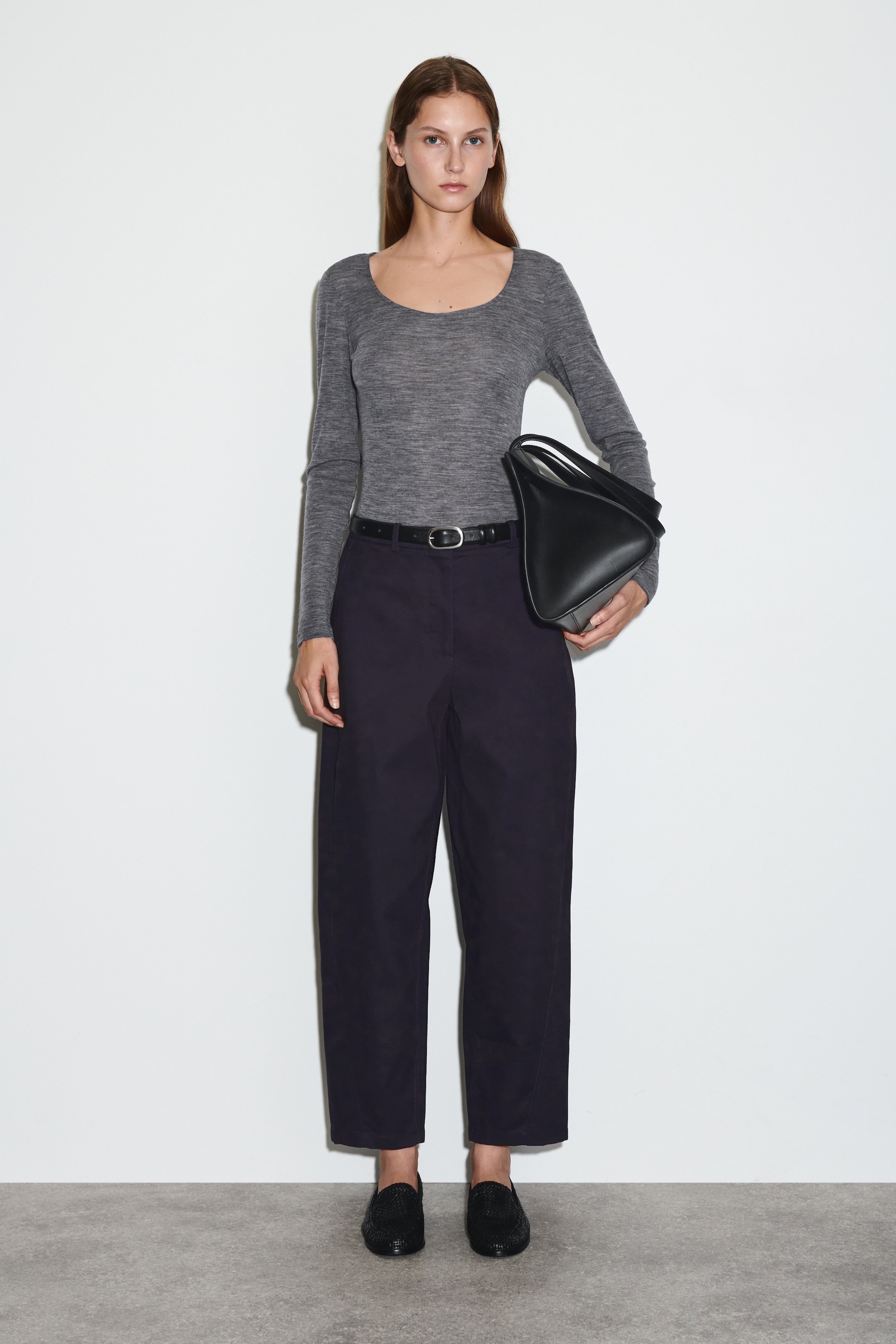 Agrandir l'image: Vue de FACE de chinos bleu marine à jambes larges avec des coutures orientées vers l'avant qui accentuent leur silhouette arrondie, et sont stylisés avec une ceinture noire et une boucle argentée.