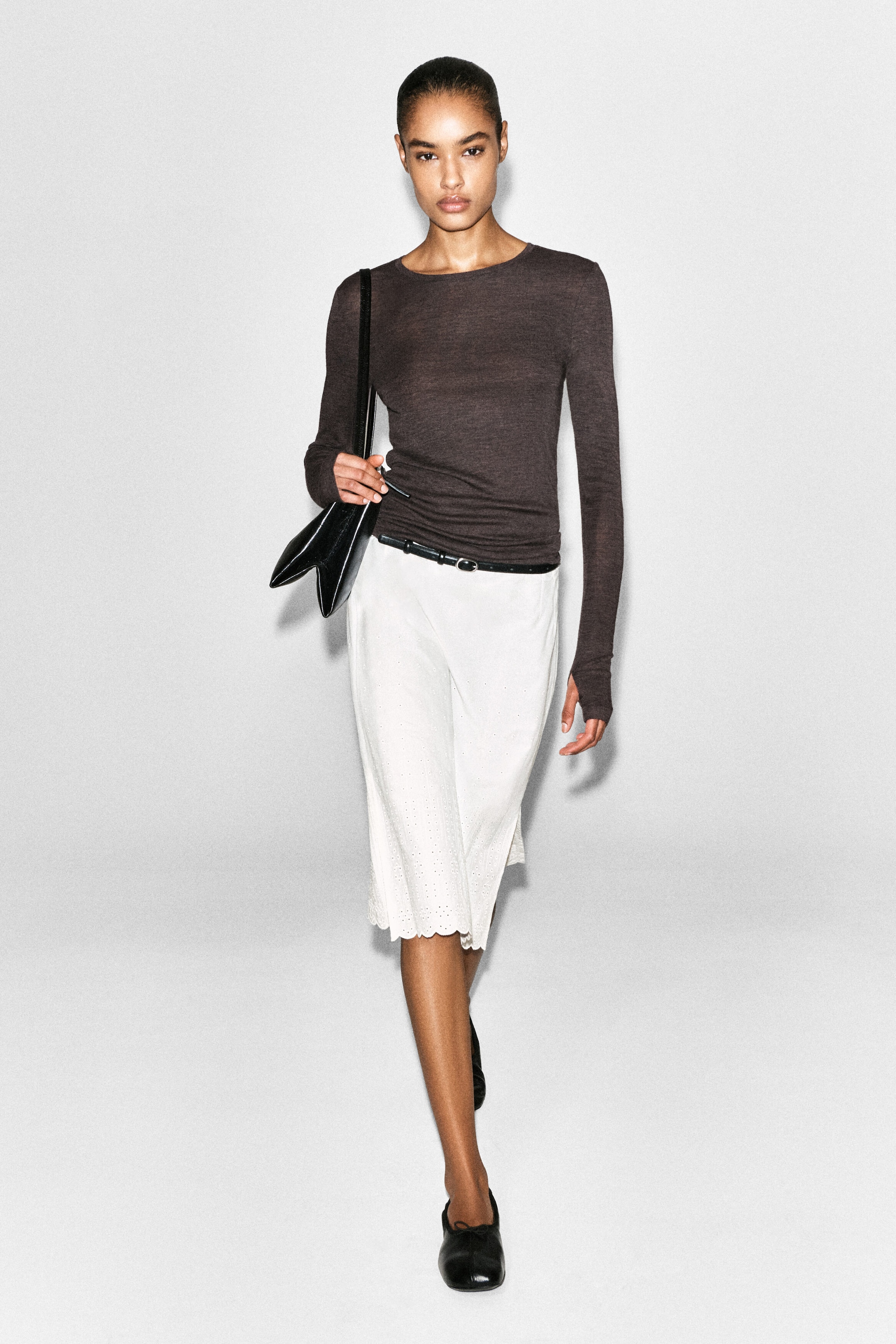 The slim merino wool top is shown from the front, featuring a dark brown, lightweight fine-knit texture and a form-fitting silhouette. It is designed with a classic crew neckline and extra-long sleeves extending over the hands, with the hem tucked into a belted white skirt to demonstrate its close fit. The slim merino wool top is shown from the front, featuring a dark brown, lightweight fine-knit texture and a form-fitting silhouette. It is designed with a classic crew neckline and extra-long sleeves extending over the hands, with the hem tucked into a belted white skirt to demonstrate its close fit.