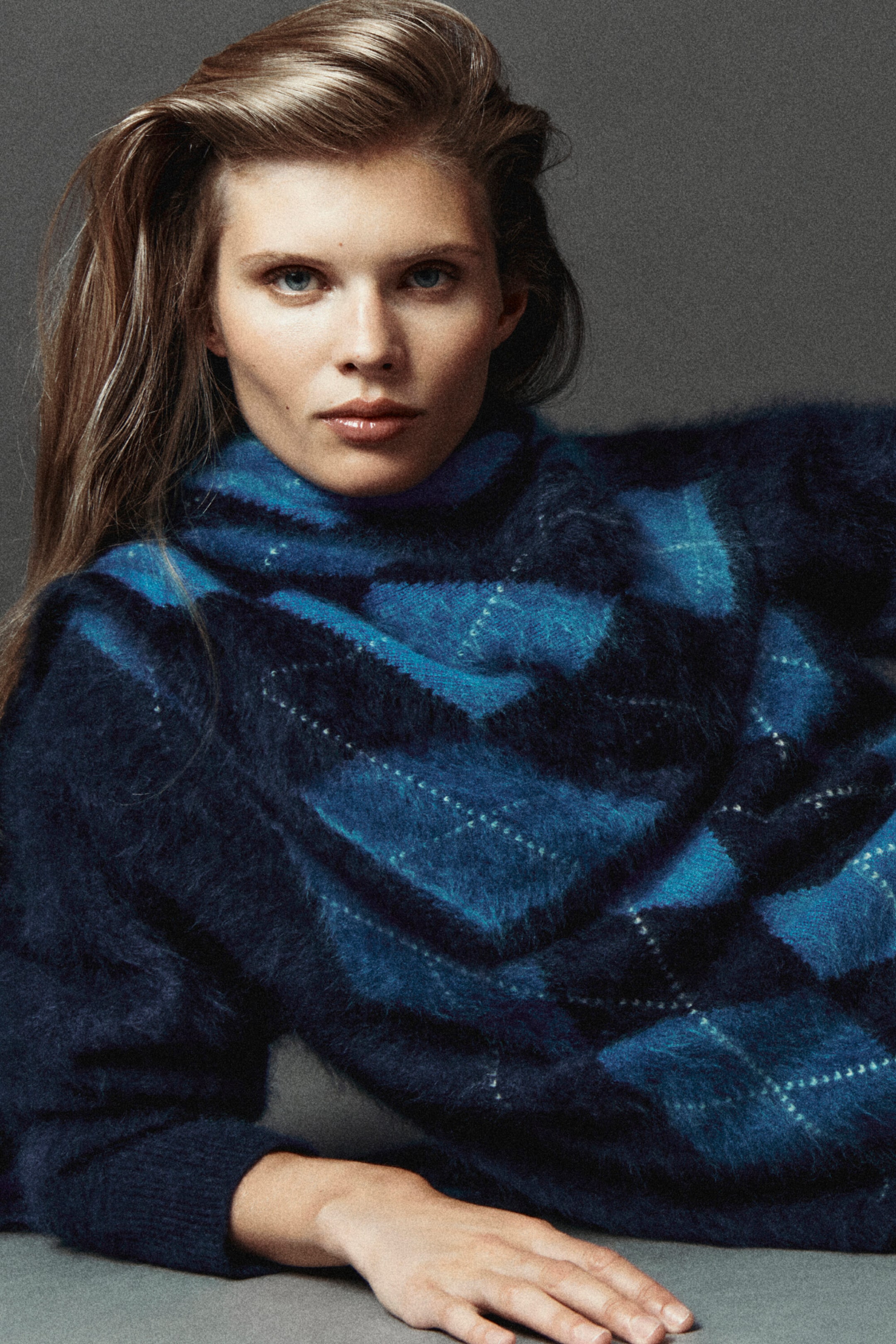 A model facing front is wearing a matching brushed cashmere jumper and triangular scarf set featuring a modern argyle pattern in shades of blue. The fuzzy-textured knitwear is styled with the triangular scarf layered over the funnel-neck jumper, highlighting the cohesive design. A model facing front is wearing a matching brushed cashmere jumper and triangular scarf set featuring a modern argyle pattern in shades of blue. The fuzzy-textured knitwear is styled with the triangular scarf layered over the funnel-neck jumper, highlighting the cohesive design.