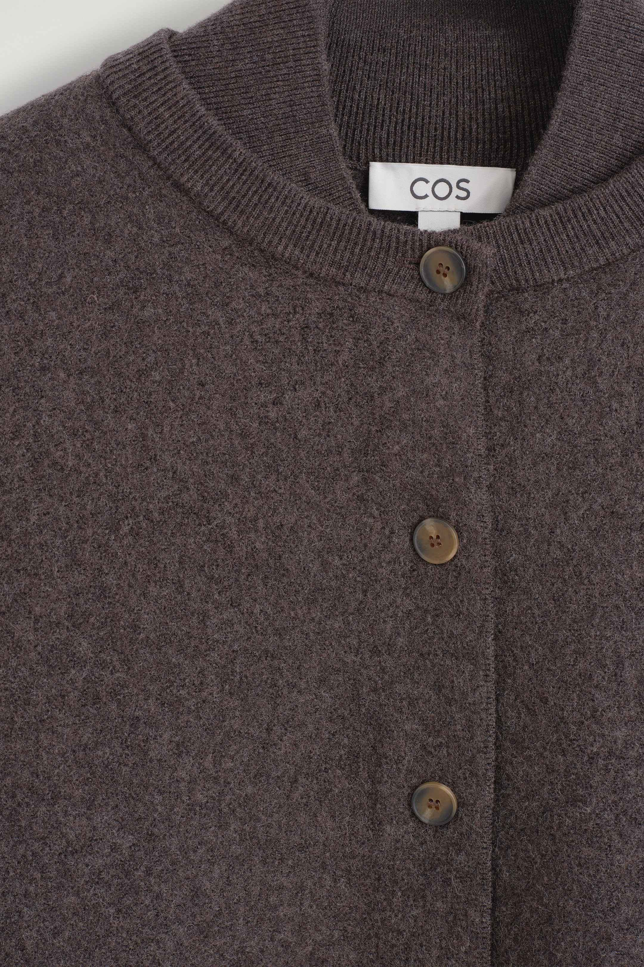 Ce gros plan montre un cardigan en laine bouillie brun foncé, doté d'un tricot texturé, d'un col côtelé à effet superposé et d'une fermeture à boutons sur le devant avec des boutons marbrés. Ce gros plan montre un cardigan en laine bouillie brun foncé, doté d'un tricot texturé, d'un col côtelé à effet superposé et d'une fermeture à boutons sur le devant avec des boutons marbrés.