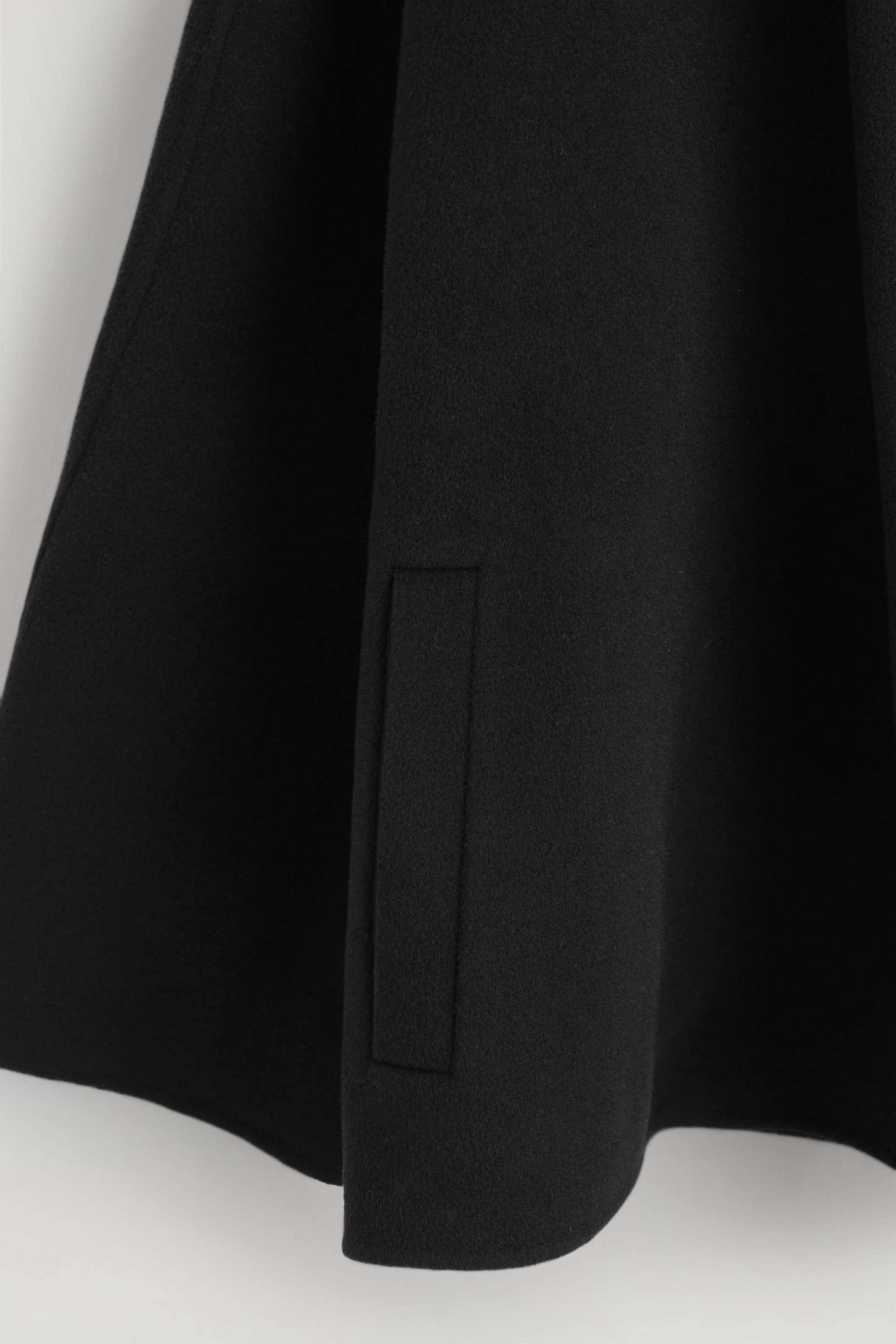 A close-up of a black wool-blend jacket showcases a vertical welt pocket and the soft drape of its double-faced fabric.