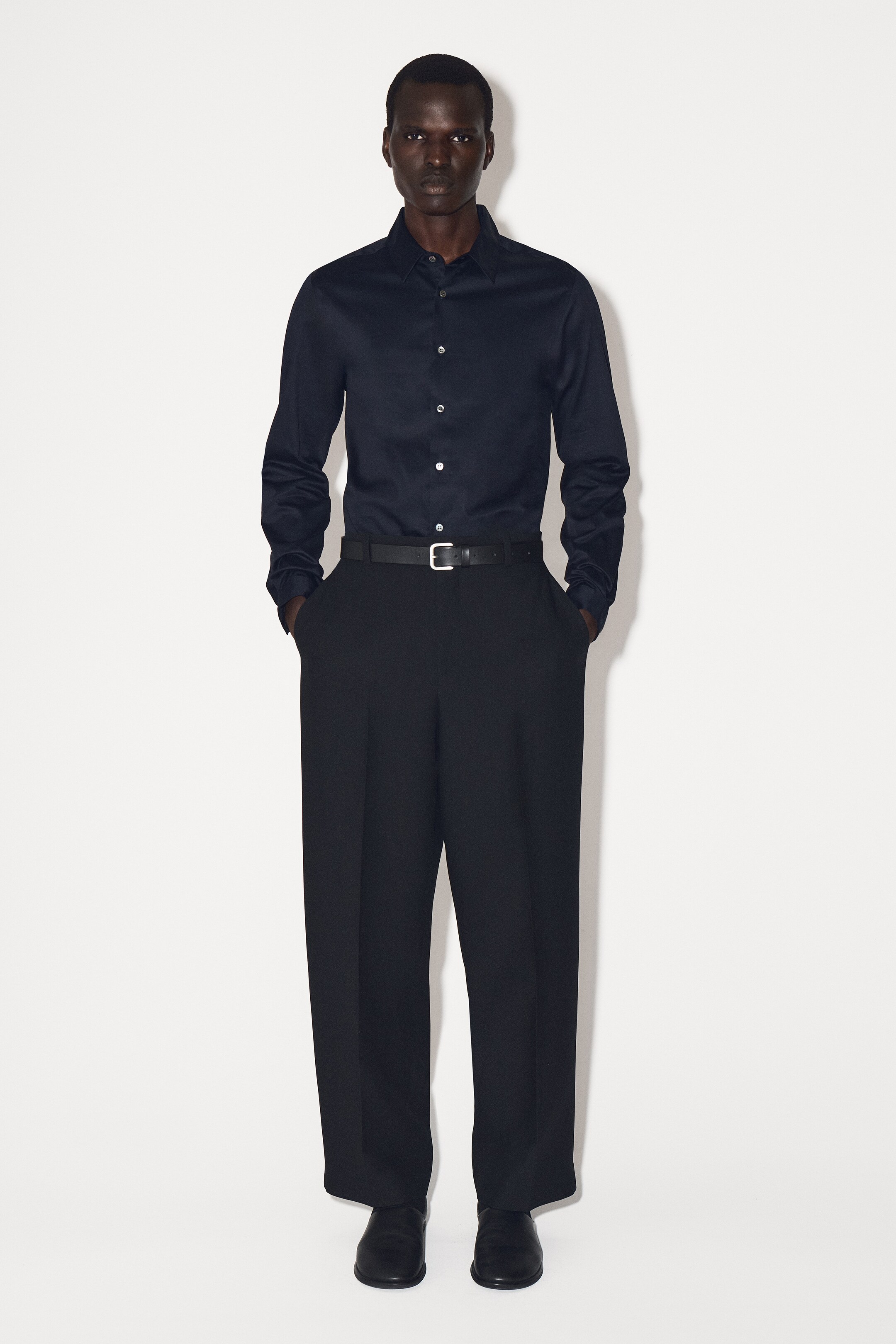 Größeres Bild anzeigen: Ein dunkelblaues Slim-Fit-Hemd wird von vorne präsentiert, mit einem spitzen Kragen, einem Knopfverschluss mit Perlmuttknöpfen vorne und langen Ärmeln mit Manschetten. Das Hemd wird in dunkle Hosen gesteckt getragen.