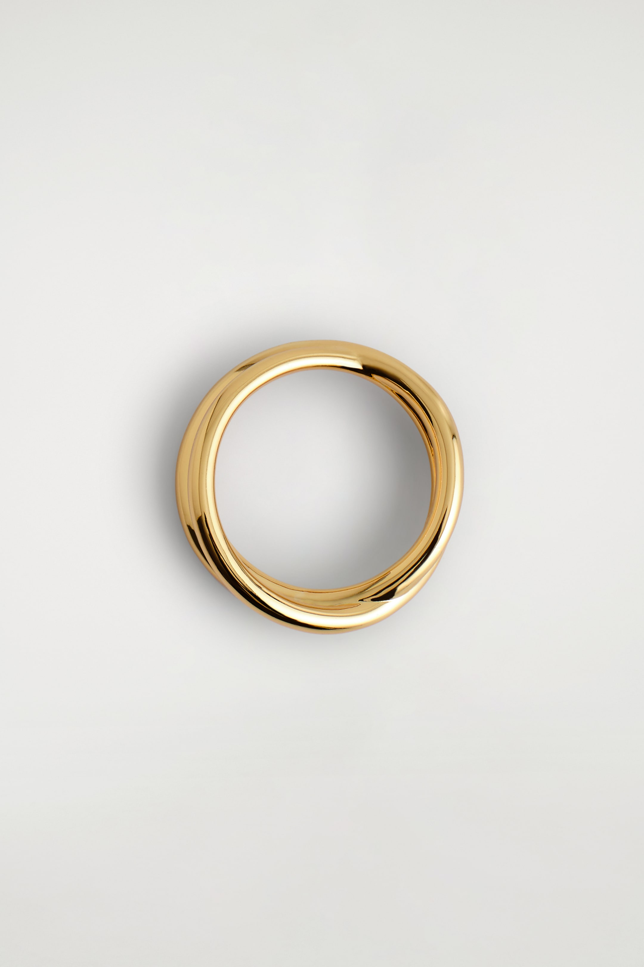 Grösseres Bild ansehen: Ein goldfarbener Ring wird aus der Vogelperspektive präsentiert, mit einem wellenförmigen, doppelten Wickeldesign und einer glatten, polierten Oberfläche.