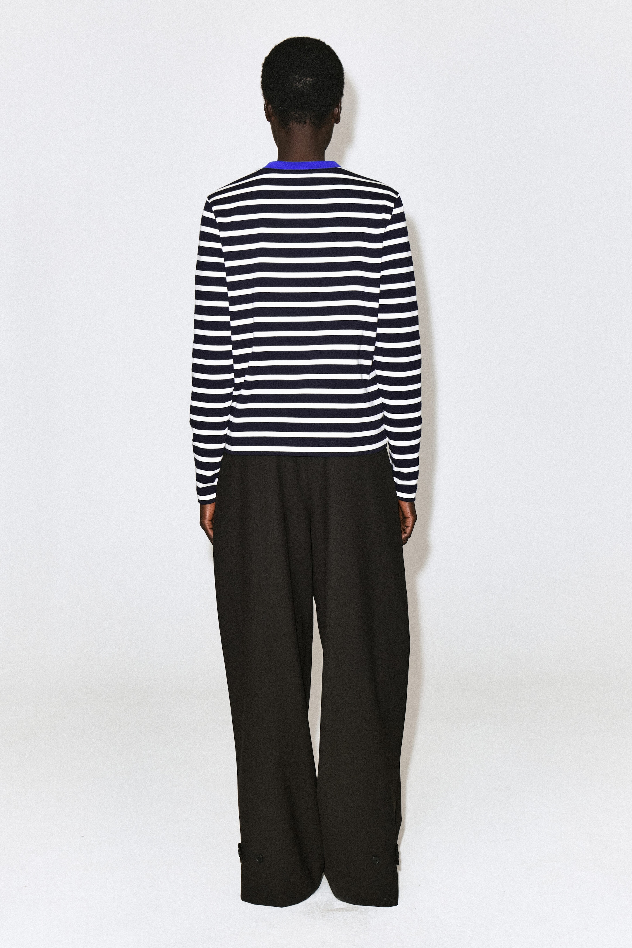Ein schlicht geschnittenes Langarm-T-Shirt mit horizontalen navy- und weißen Streifen sowie einem kontrastierenden leuchtend blauen Rundhalsausschnitt wird vom Model von hinten getragen. Das T-Shirt ist mit schwarzen Wide-Leg-Hosen kombiniert. Ein schlicht geschnittenes Langarm-T-Shirt mit horizontalen navy- und weißen Streifen sowie einem kontrastierenden leuchtend blauen Rundhalsausschnitt wird vom Model von hinten getragen. Das T-Shirt ist mit schwarzen Wide-Leg-Hosen kombiniert.