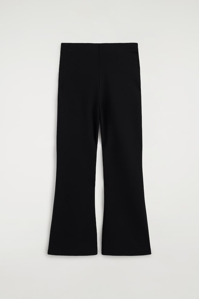 Black trousers feature a flat waistband and a slim fit through the thigh, flaring out at the bottom. - 1