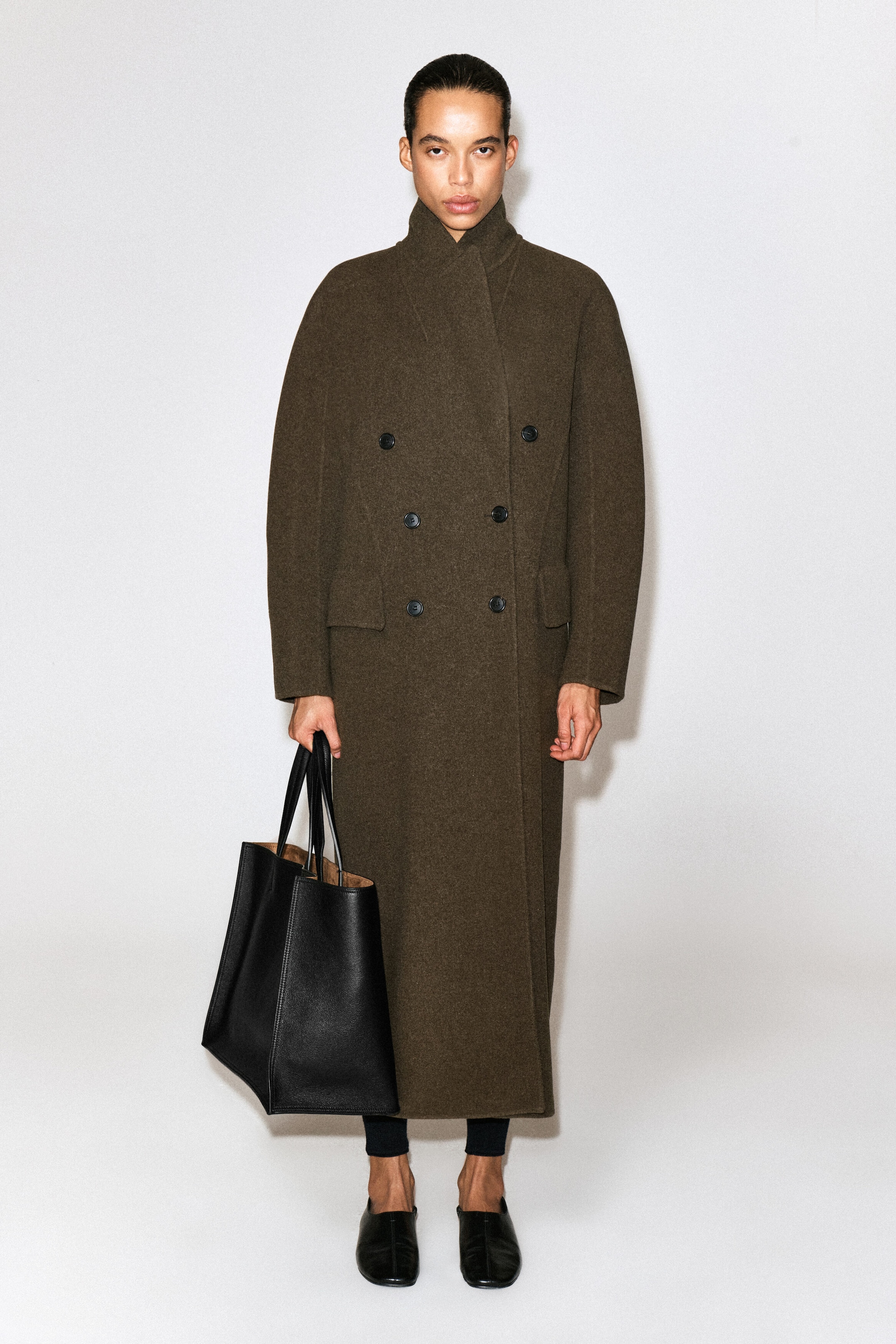 The black leather tote bag is being held facing forward, showcasing its structured silhouette, soft-grain texture, and dual top handles. The open top reveals a contrasting tan bonded lining, highlighting its spacious design. The black leather tote bag is being held facing forward, showcasing its structured silhouette, soft-grain texture, and dual top handles. The open top reveals a contrasting tan bonded lining, highlighting its spacious design.
