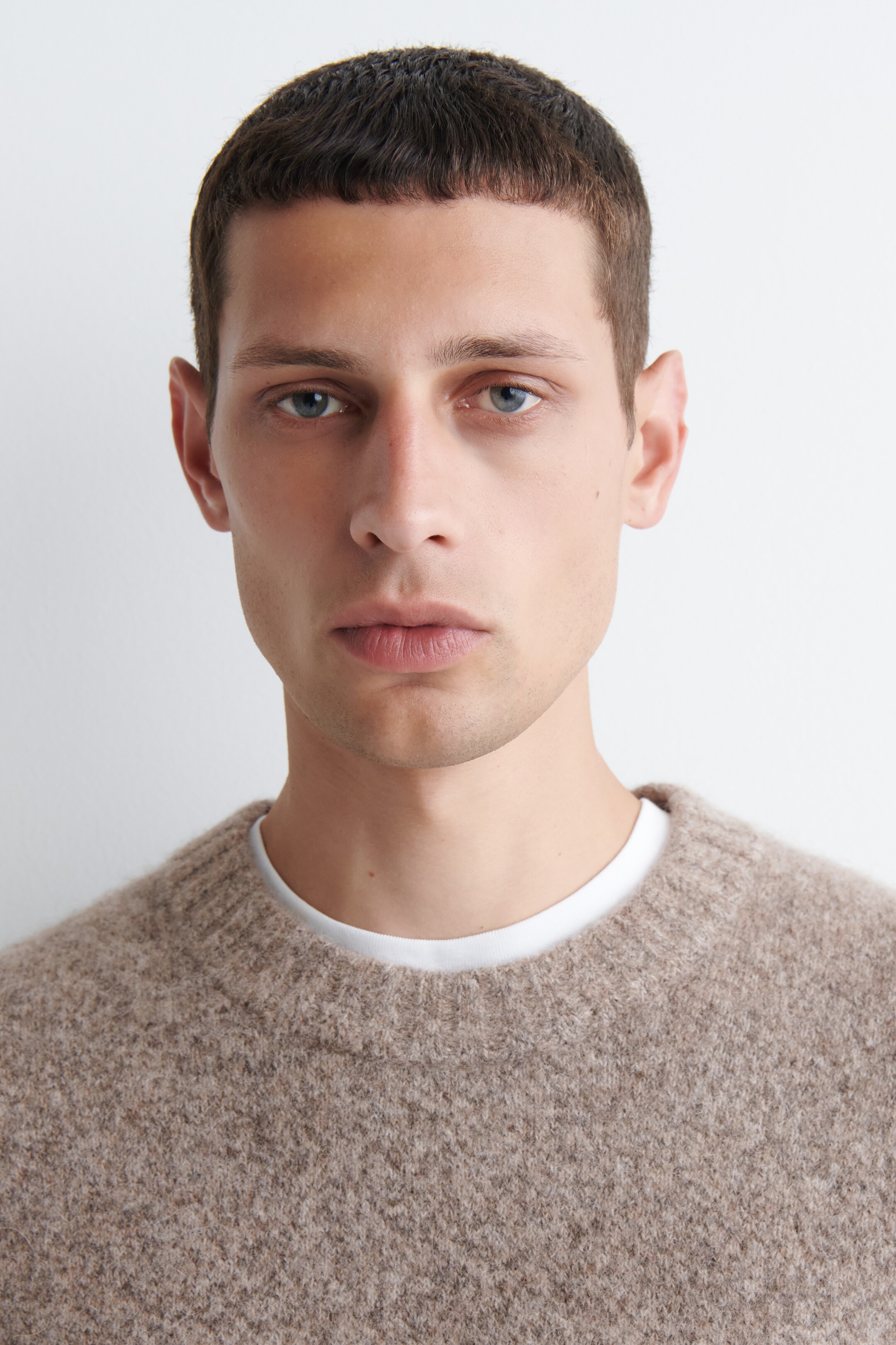 Ver imagen más grande: Un suéter beige de cuello redondo de mezcla melange se está usando, de frente, mostrando su suave textura de punto cepillado. Se ve una camiseta blanca debajo en el escote, creando un aspecto de capas.