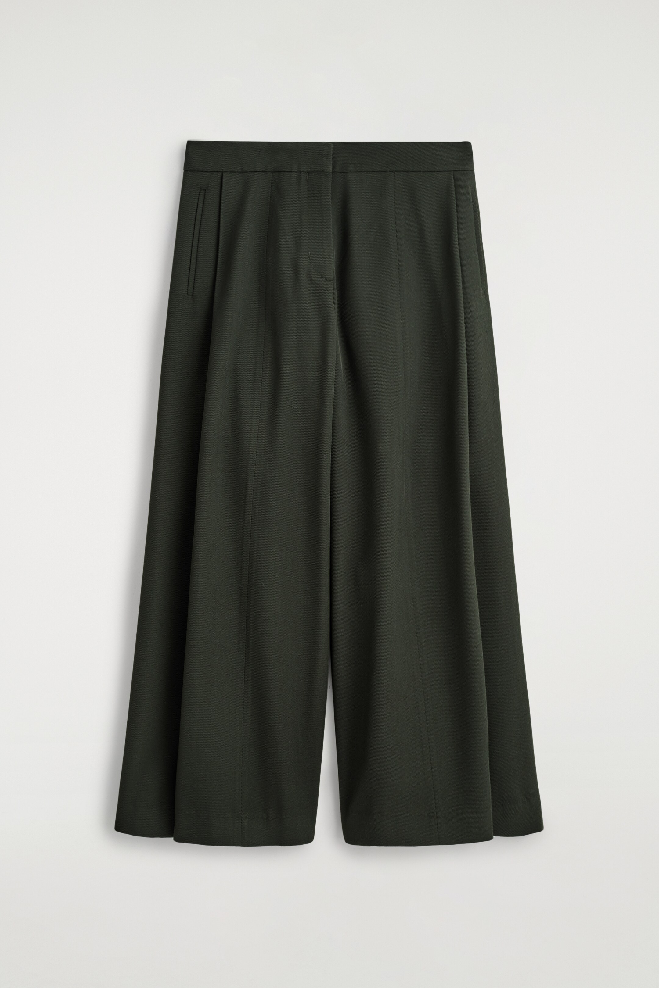 Visualizza immagine più grande: Un paio di pantaloni a gamba larga di colore verde scuro è mostrato come FRONTE, con una cintura pulita, una singola tasca a filetto visibile sul lato sinistro e pieghe verticali prominenti che scendono lungo la parte anteriore di ciascuna gamba.