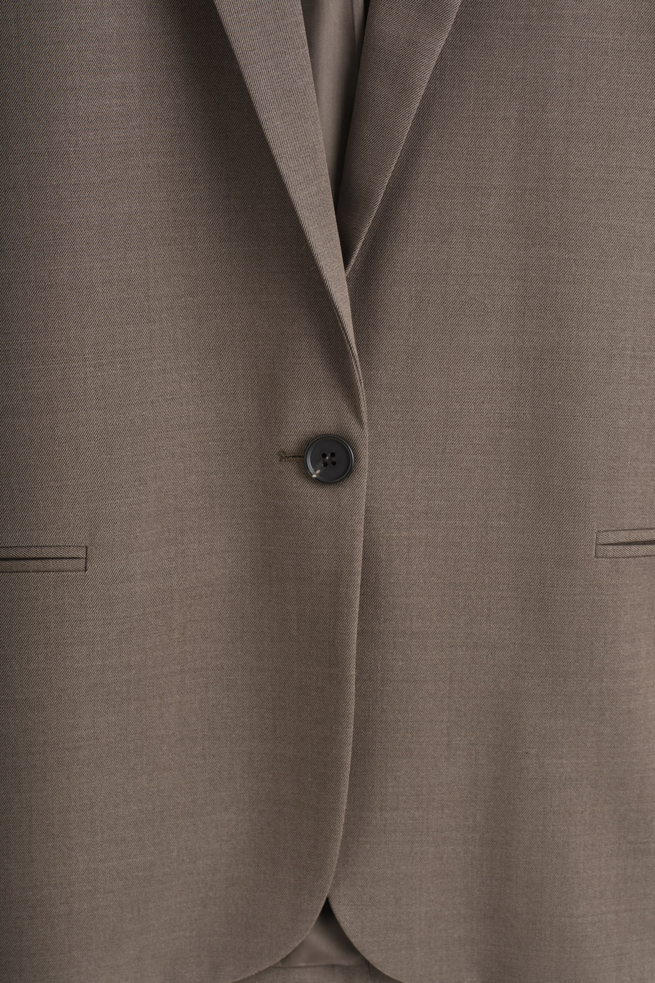 Ver imagem maior: Um blazer taupe de abotoamento simples está a ser mostrado de FRENTE, apresentando um padrão diagonal subtil, um único botão escuro, lapelas alongadas e dois bolsos horizontais de jato.