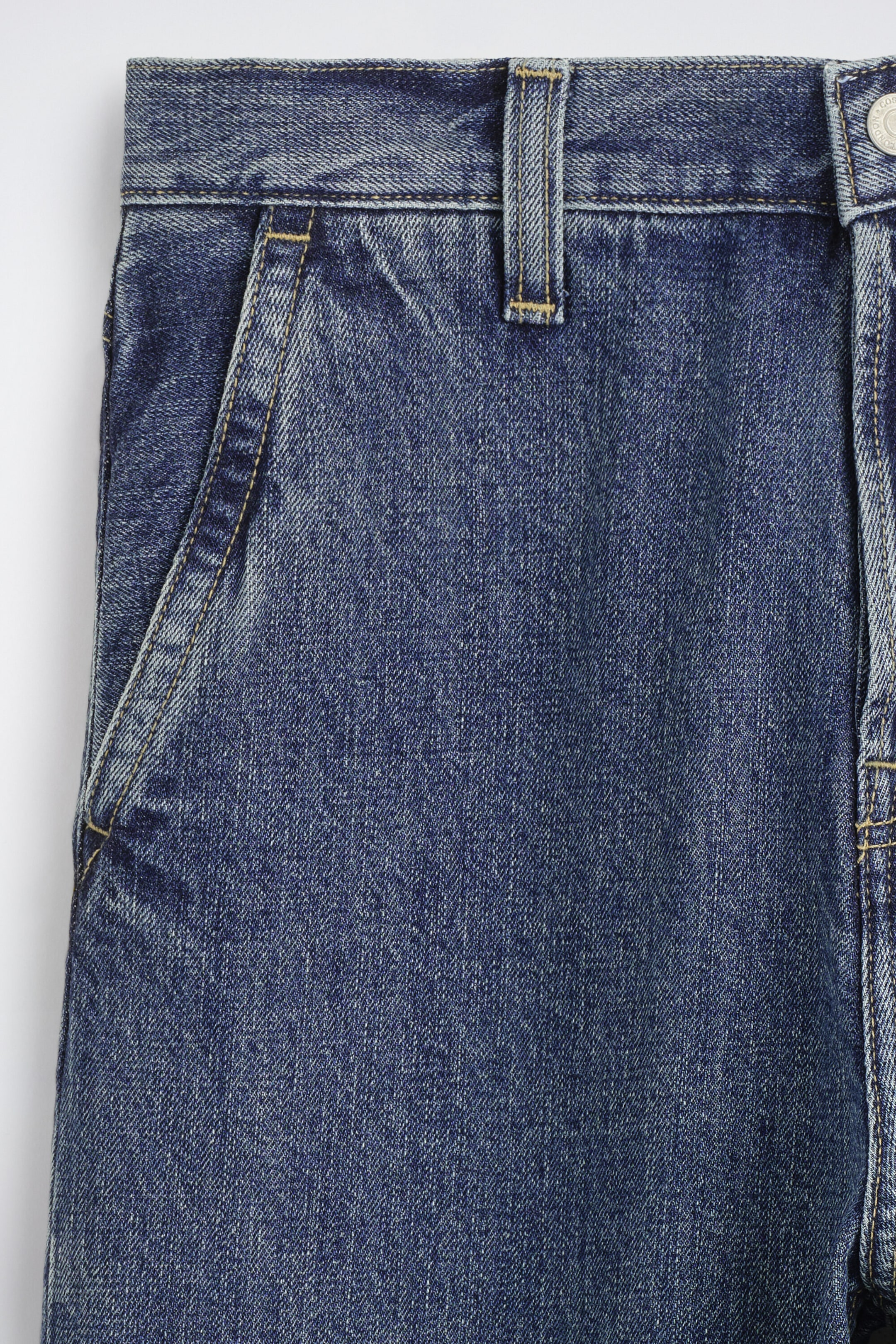 The relaxed-fit straight-leg denim trousers are shown in a close-up front view, showcasing a mid-blue wash with subtle fading. The design features a structured waistband with belt loops, contrasting yellow topstitching, and a slanted front pocket. The relaxed-fit straight-leg denim trousers are shown in a close-up front view, showcasing a mid-blue wash with subtle fading. The design features a structured waistband with belt loops, contrasting yellow topstitching, and a slanted front pocket.