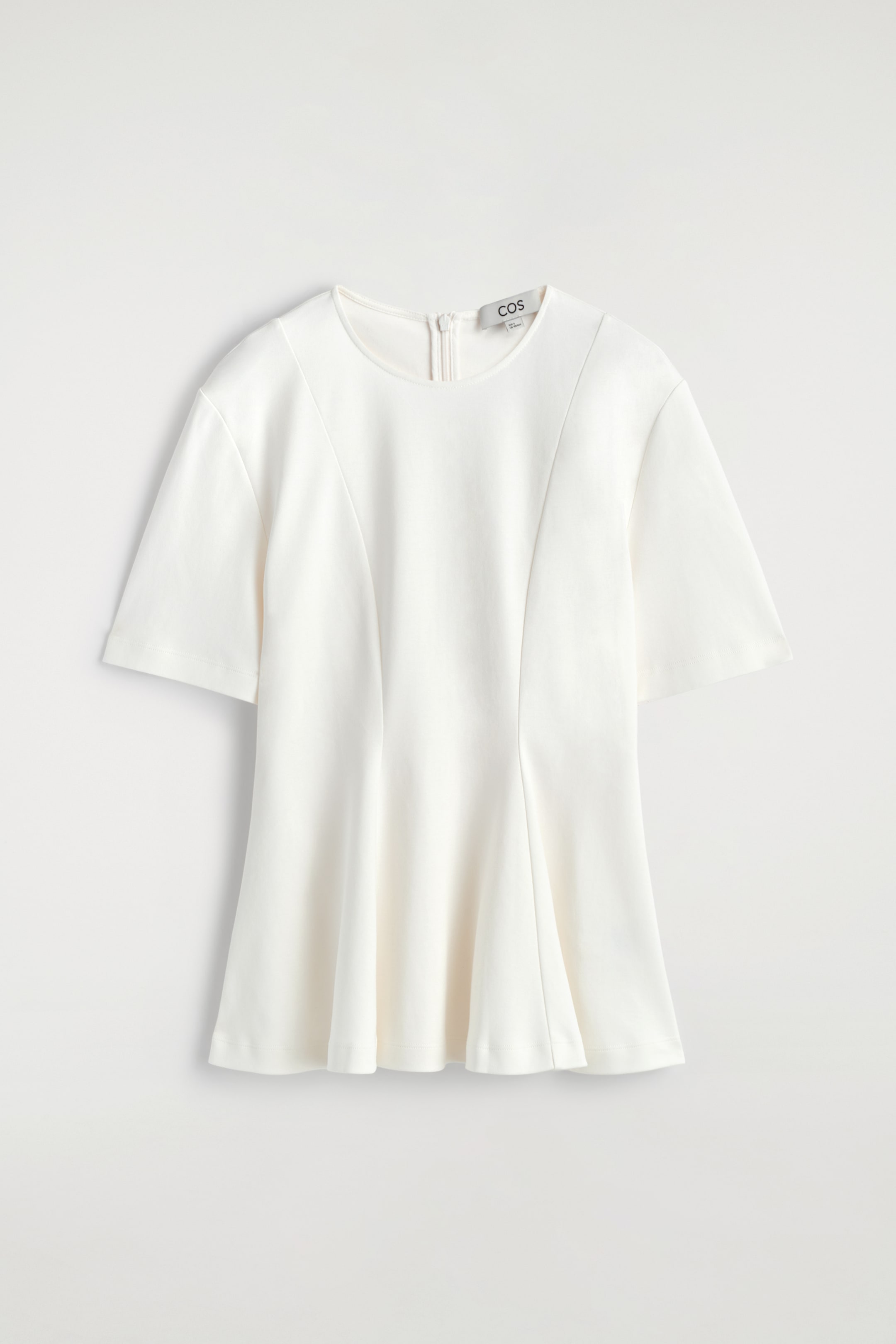 Se større billede: En hvid t-shirt præsenteres fra forsiden, med rund halsudskæring, korte ærmer og tone-i-tone coverstitch syede timeglas paneler. Disse paneler skaber en svajet silhuet, og en lynlås lukning er synlig ved baghalsudskæringen.