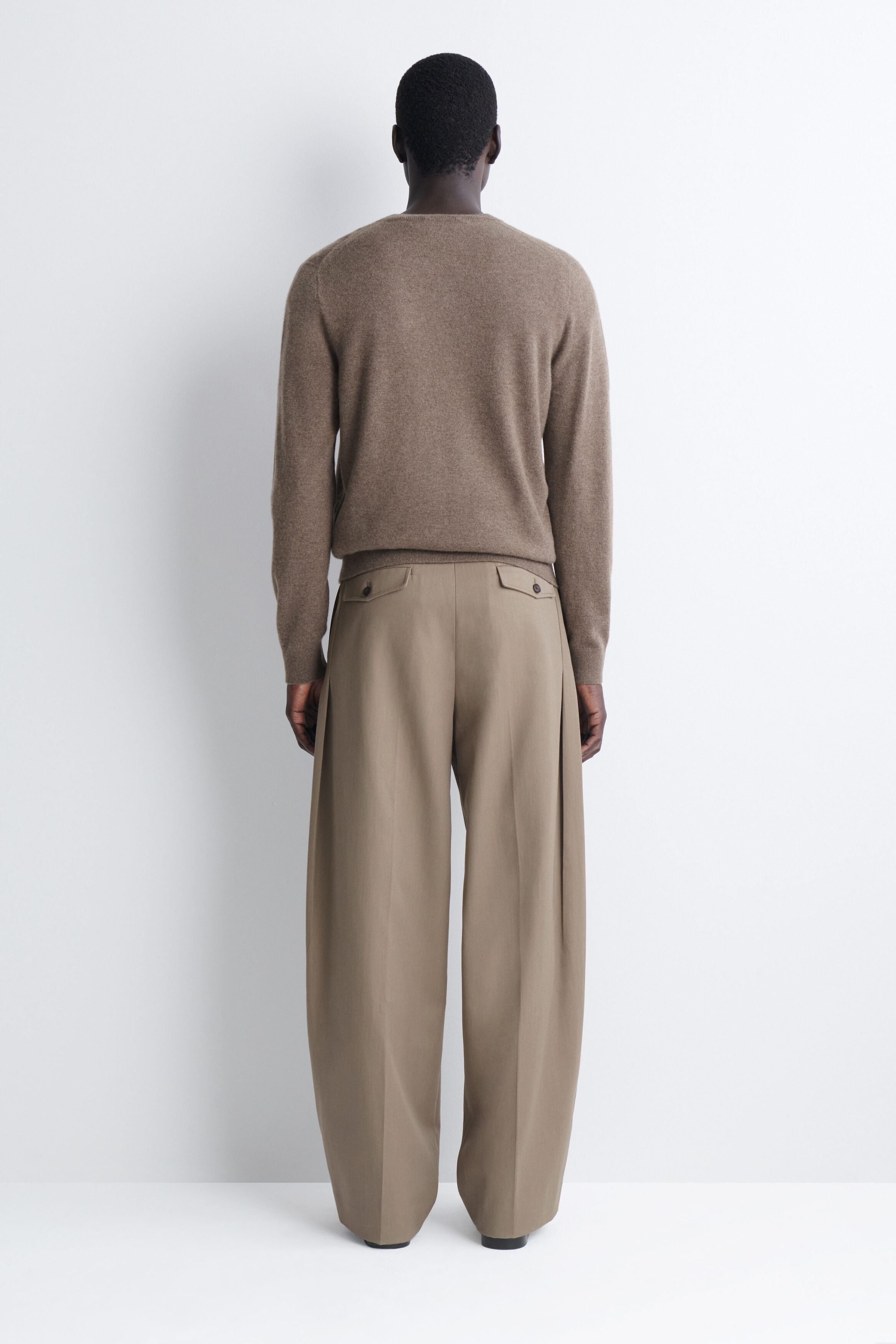 Mostrando la vista trasera, estos pantalones anchos de color topo presentan una caída relajada con marcas centrales marcadas y bolsillos traseros de ojal con solapas abotonadas, combinados con un jersey de punto marrón de manga larga. Mostrando la vista trasera, estos pantalones anchos de color topo presentan una caída relajada con marcas centrales marcadas y bolsillos traseros de ojal con solapas abotonadas, combinados con un jersey de punto marrón de manga larga.