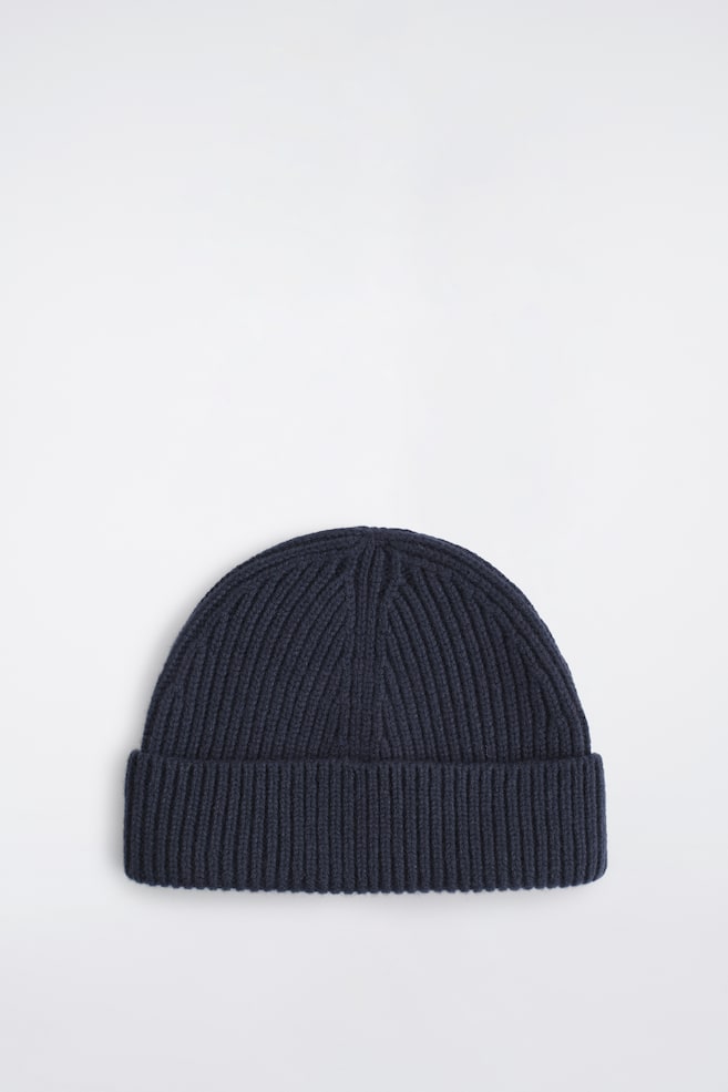Un gorro de lana grueso de canalé en azul marino oscuro, visto de frente, muestra su textura de punto acanalado grueso y un amplio dobladillo vuelto. El gorro presenta una copa redondeada con visibles lÃneas de disminución del tejido que se estrechan hacia el centro superior. - 1