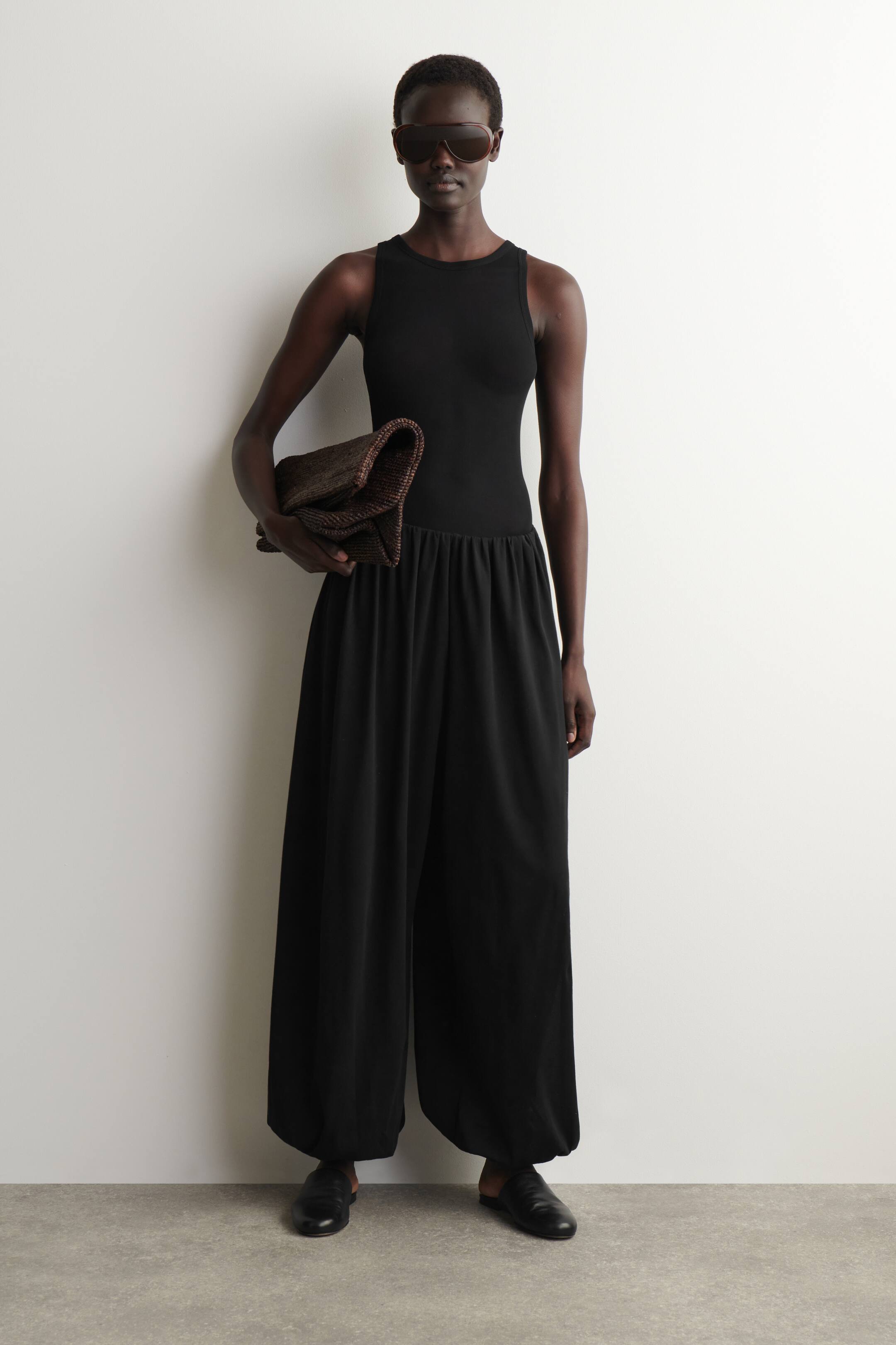 Agrandir l'image: Une combinaison noire sans manches présente un haut ajusté avec un col rond, et un pantalon large et fluide resserré à la taille et aux chevilles.