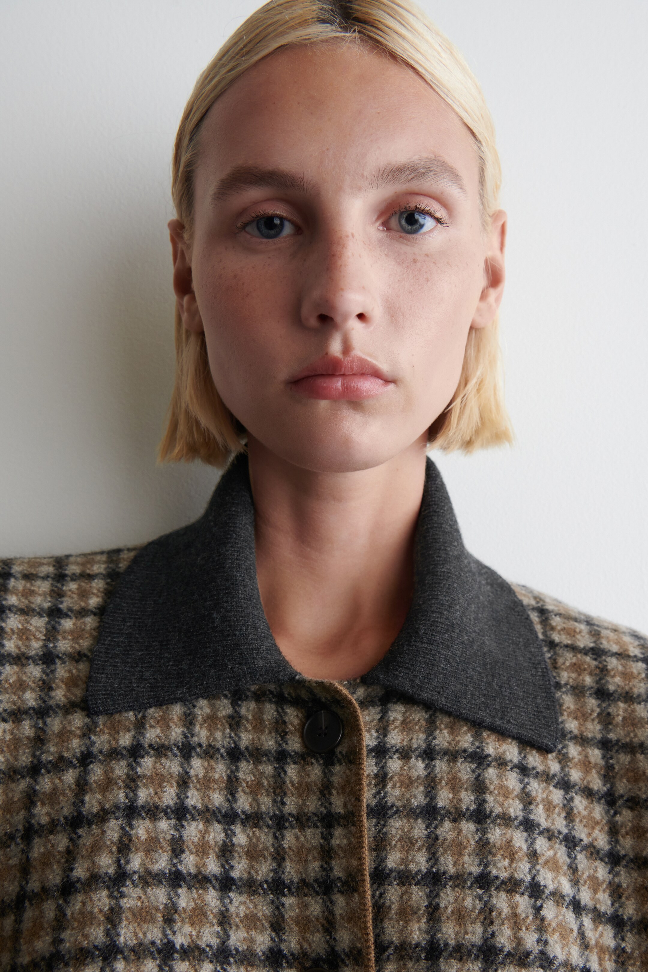 View larger image: A jacket in a brown, black, and beige plaid pattern is being shown. It features a contrasting dark grey spread collar and a visible black button closure on its front placket.