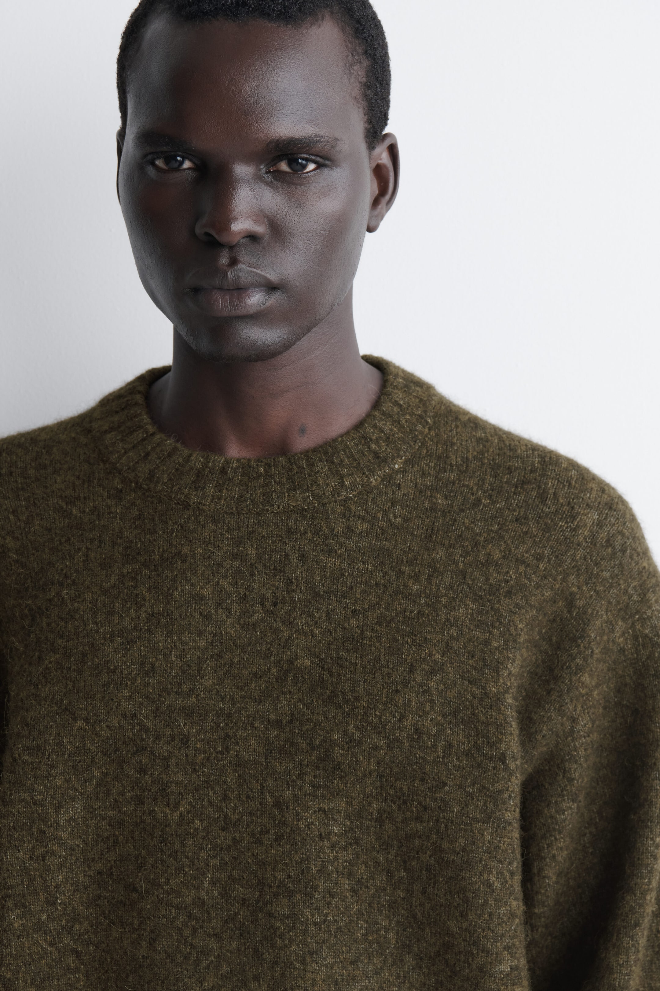 An oversized alpaca-blend crew-neck jumper is shown in a close-up front view, highlighting its fuzzy, textured knit in a dark olive-green hue and its thick ribbed crew neckline. An oversized alpaca-blend crew-neck jumper is shown in a close-up front view, highlighting its fuzzy, textured knit in a dark olive-green hue and its thick ribbed crew neckline.