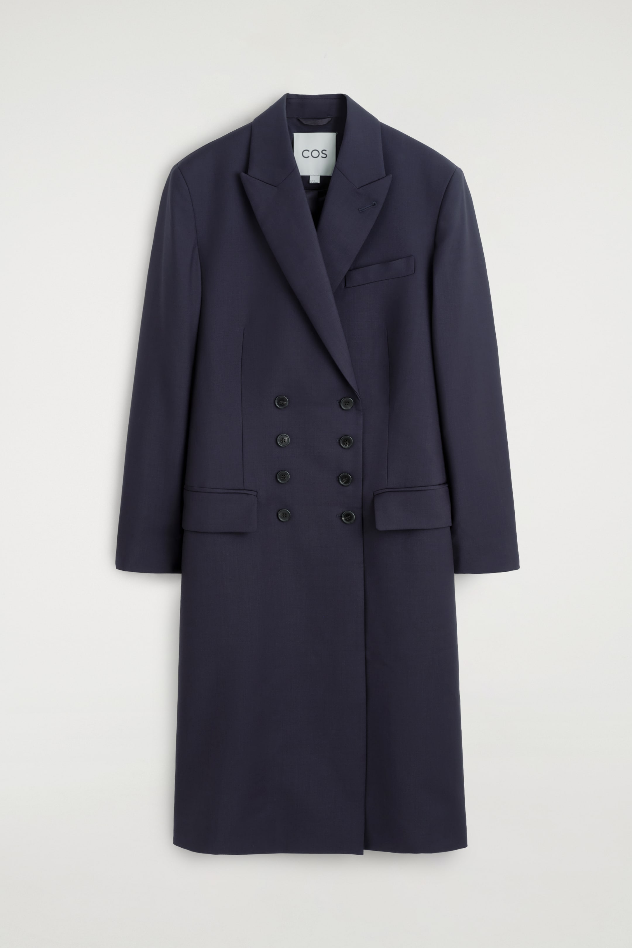 Ver imagen más grande: Un blazer largo cruzado de color azul marino oscuro está colgado de frente, mostrando su diseño estructurado. El blazer presenta solapas de pico afiladas, un bolsillo de ribete en el pecho, dos bolsillos laterales con solapa y un cierre frontal de ocho botones.