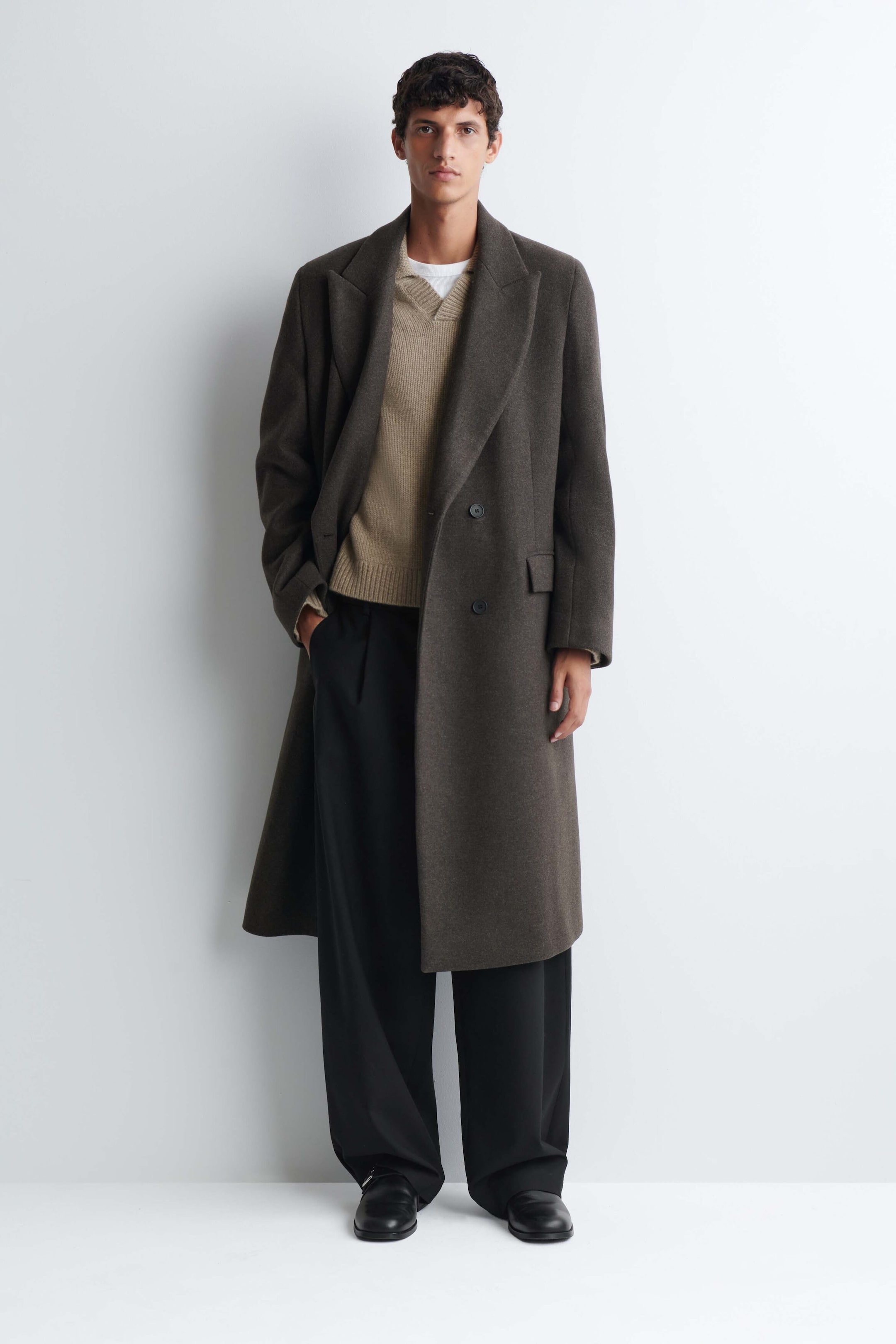 The chunky cashmere polo sweater in beige is worn by the model, layered over a white T-shirt and under a long, dark gray double-breasted overcoat. The knit sweater features an open polo collar and a ribbed hem, and is styled with wide-leg black trousers. The chunky cashmere polo sweater in beige is worn by the model, layered over a white T-shirt and under a long, dark gray double-breasted overcoat. The knit sweater features an open polo collar and a ribbed hem, and is styled with wide-leg black trousers.