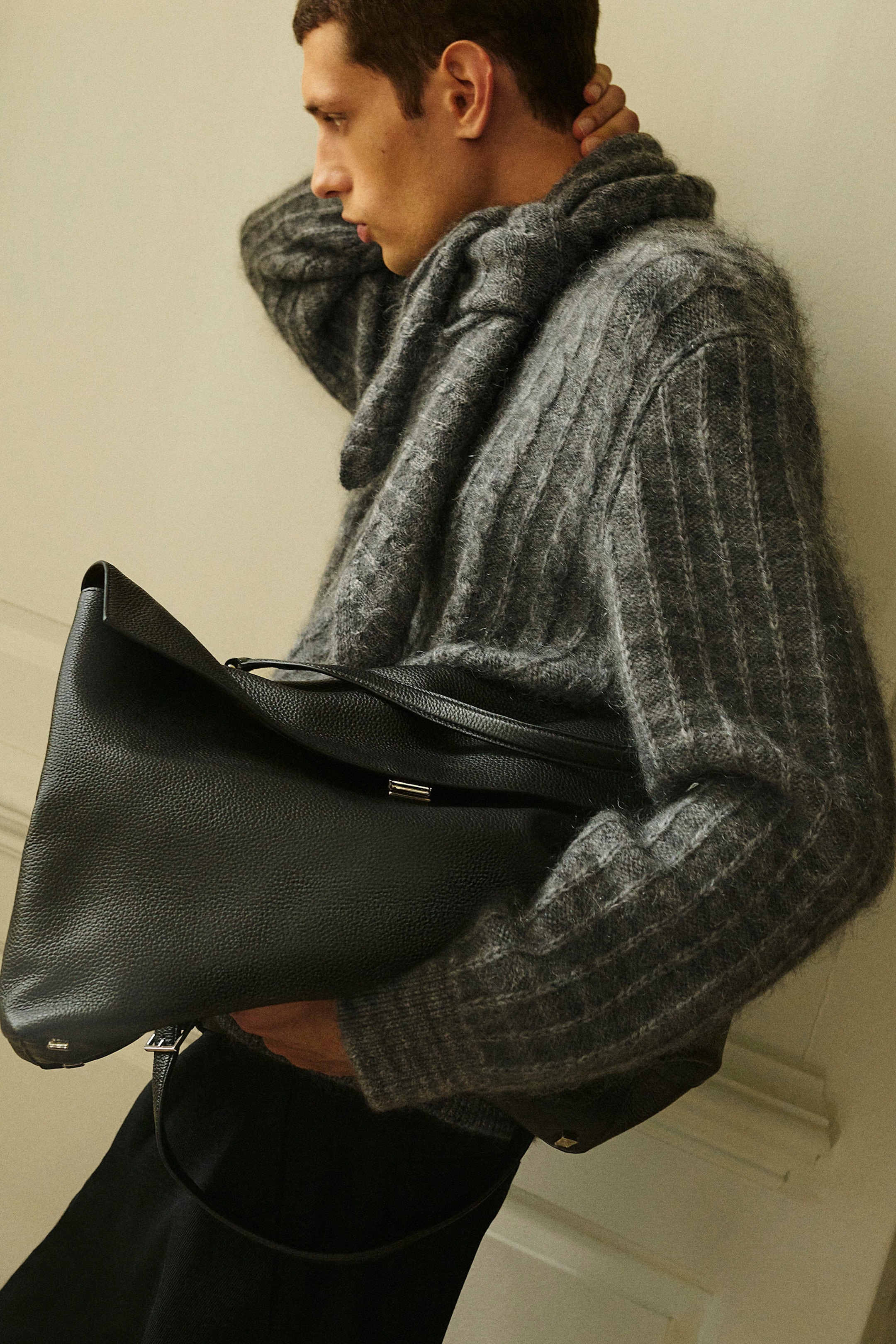 Una modella indossa un maglione in merino-mohair grigio lavorato a trecce e una sciarpa triangolare coordinata a righe a quadri lavorata a trecce, mostrati in una vista di profilo laterale. Il maglione presenta una lavorazione a maglia soffice e testurizzata con polsini a coste, mentre la sciarpa è drappeggiata intorno al collo e una grande borsa in pelle nera è tenuta sotto il braccio. Una modella indossa un maglione in merino-mohair grigio lavorato a trecce e una sciarpa triangolare coordinata a righe a quadri lavorata a trecce, mostrati in una vista di profilo laterale. Il maglione presenta una lavorazione a maglia soffice e testurizzata con polsini a coste, mentre la sciarpa è drappeggiata intorno al collo e una grande borsa in pelle nera è tenuta sotto il braccio.