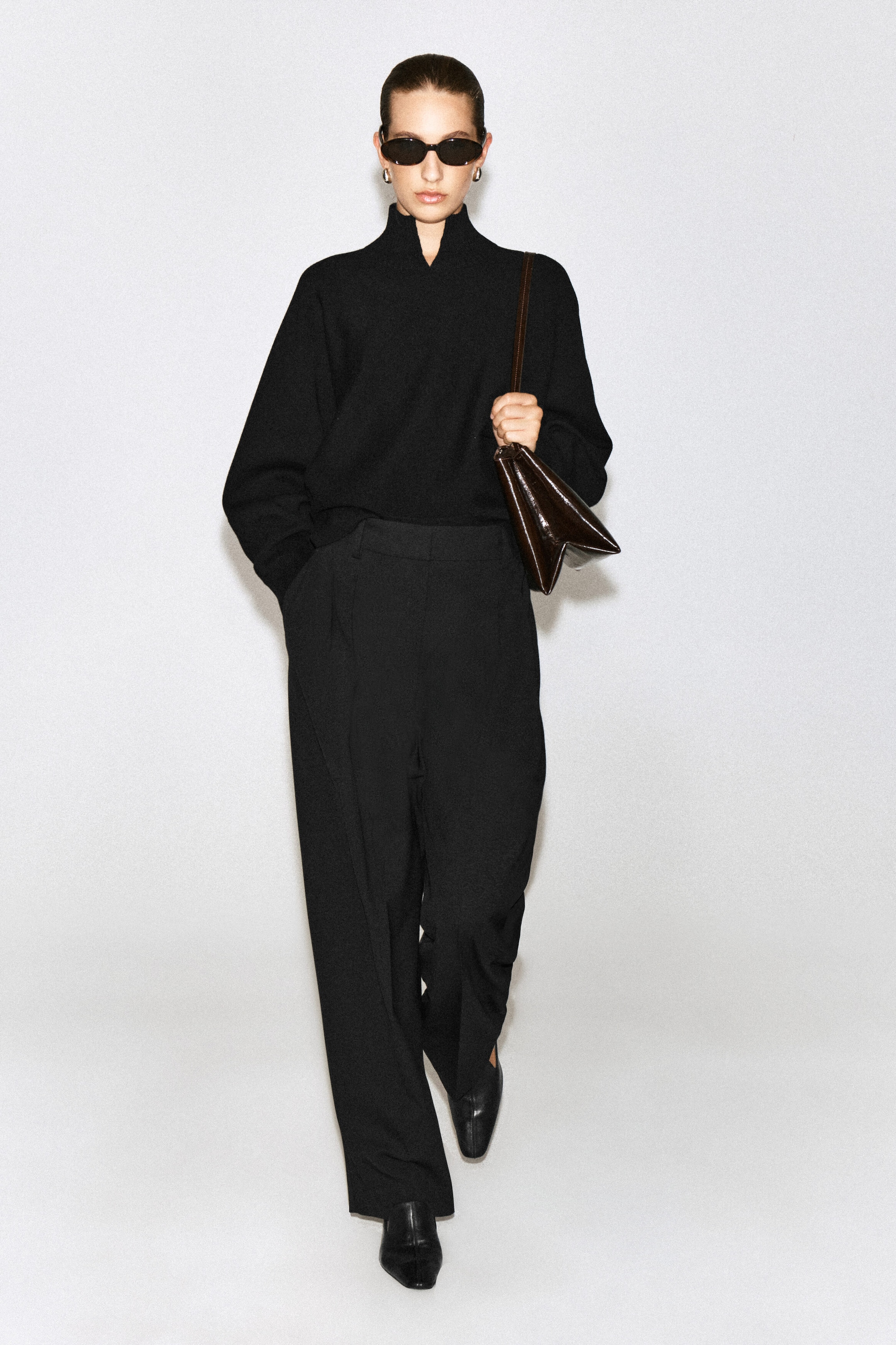 Le pull à col cheminée en laine bouillie noire avec détail en V est porté par le mannequin; il présente un col montant avec une petite ouverture en V à l’avant. Ce pull à coupe décontractée est rentré dans un pantalon noir assorti à jambe large et accompagné d’un sac à bandoulière brun foncé. Le pull à col cheminée en laine bouillie noire avec détail en V est porté par le mannequin; il présente un col montant avec une petite ouverture en V à l’avant. Ce pull à coupe décontractée est rentré dans un pantalon noir assorti à jambe large et accompagné d’un sac à bandoulière brun foncé.