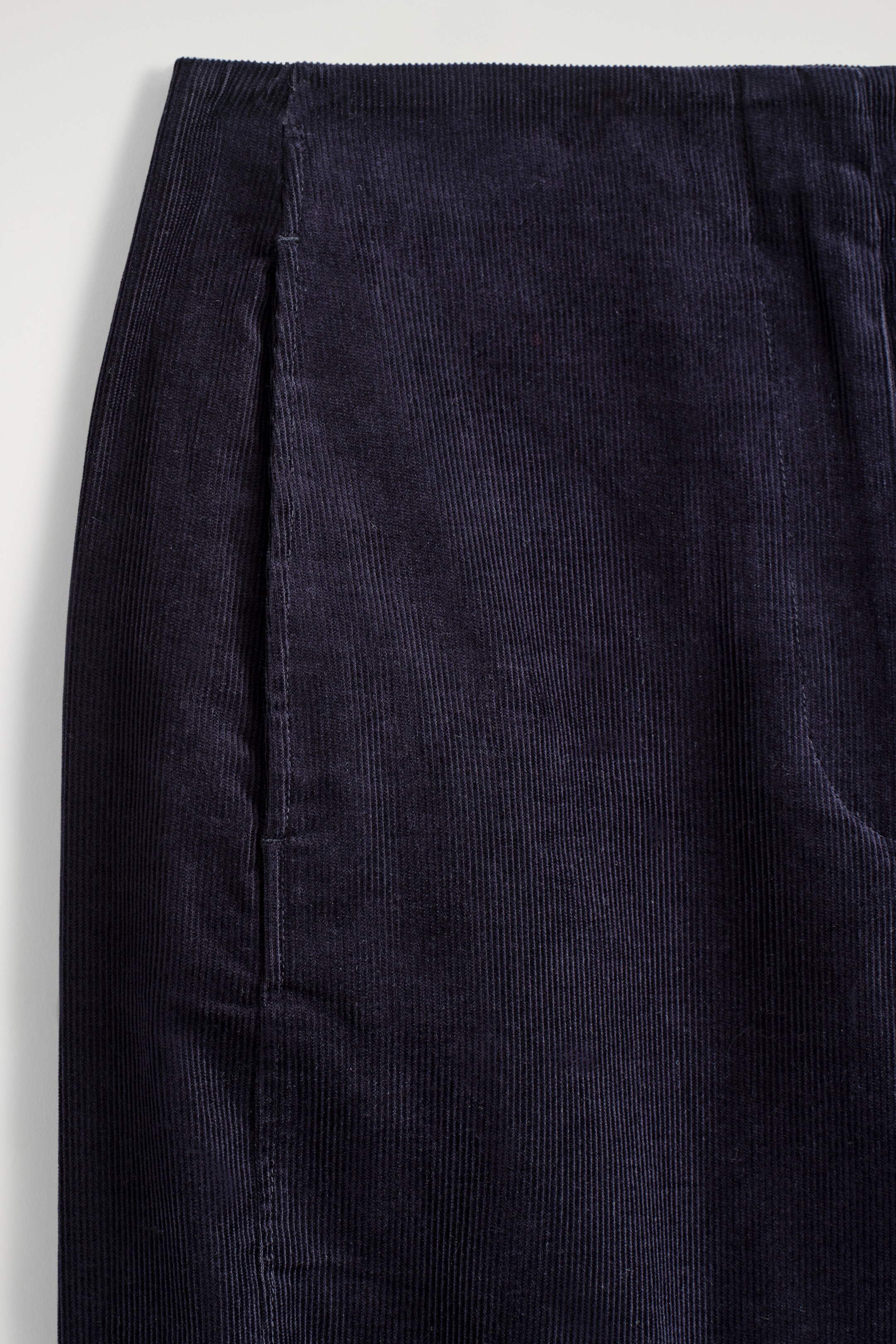 Ver imagen más grande: Los pantalones de pana azul oscuro se presentan en un primer plano, visto de frente, mostrando prominentes galones verticales. En la parte superior se puede ver una cinturilla limpia, junto con un bolsillo lateral con pespuntes tonales.