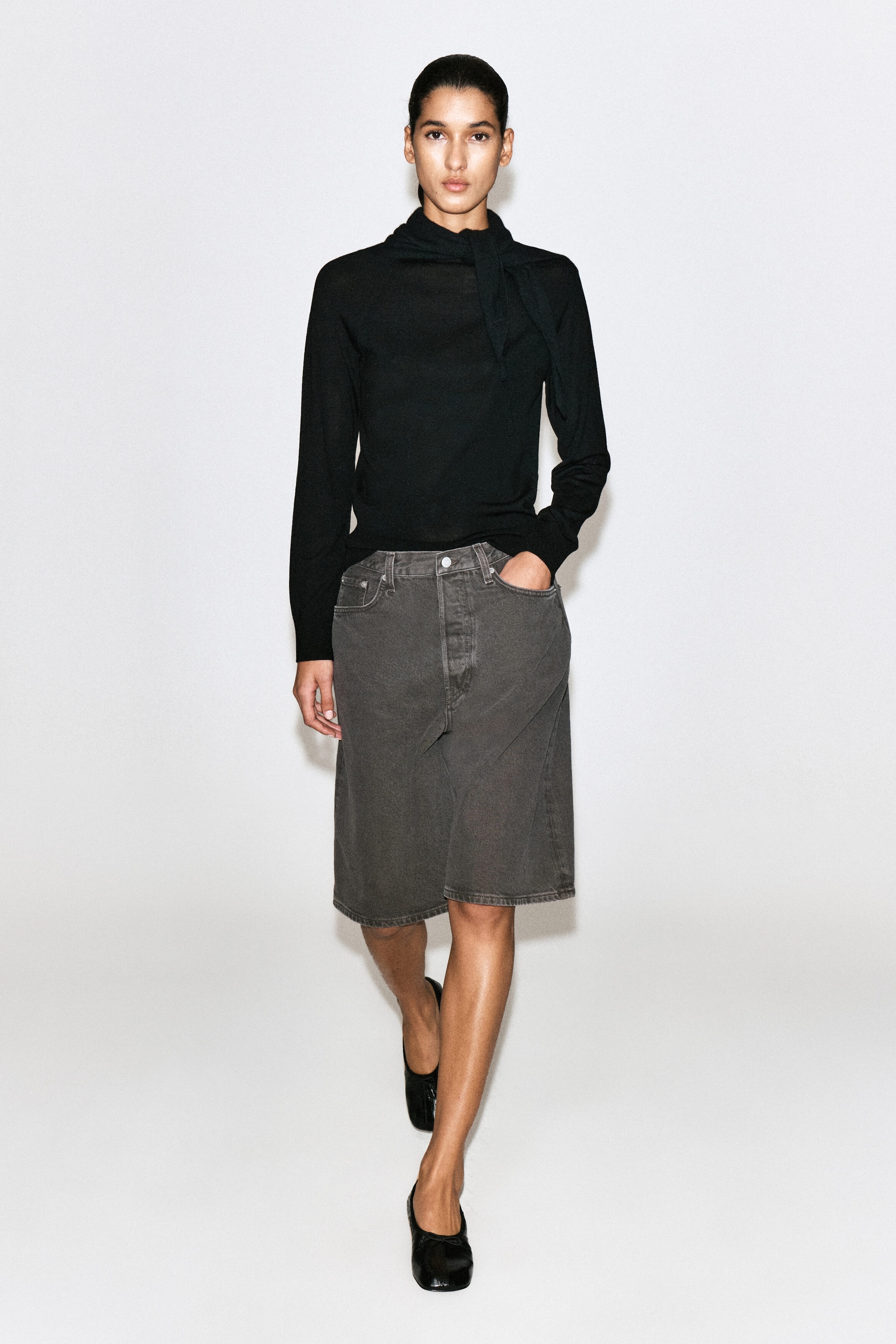 These longline denim shorts in a dark espresso wash are shown from the front, highlighting their high-rise waist and relaxed, knee-length fit. The shorts feature a classic five-pocket design with tonal topstitching and are styled with a tucked-in black long-sleeve top to emphasize the waistband structure. These longline denim shorts in a dark espresso wash are shown from the front, highlighting their high-rise waist and relaxed, knee-length fit. The shorts feature a classic five-pocket design with tonal topstitching and are styled with a tucked-in black long-sleeve top to emphasize the waistband structure.
