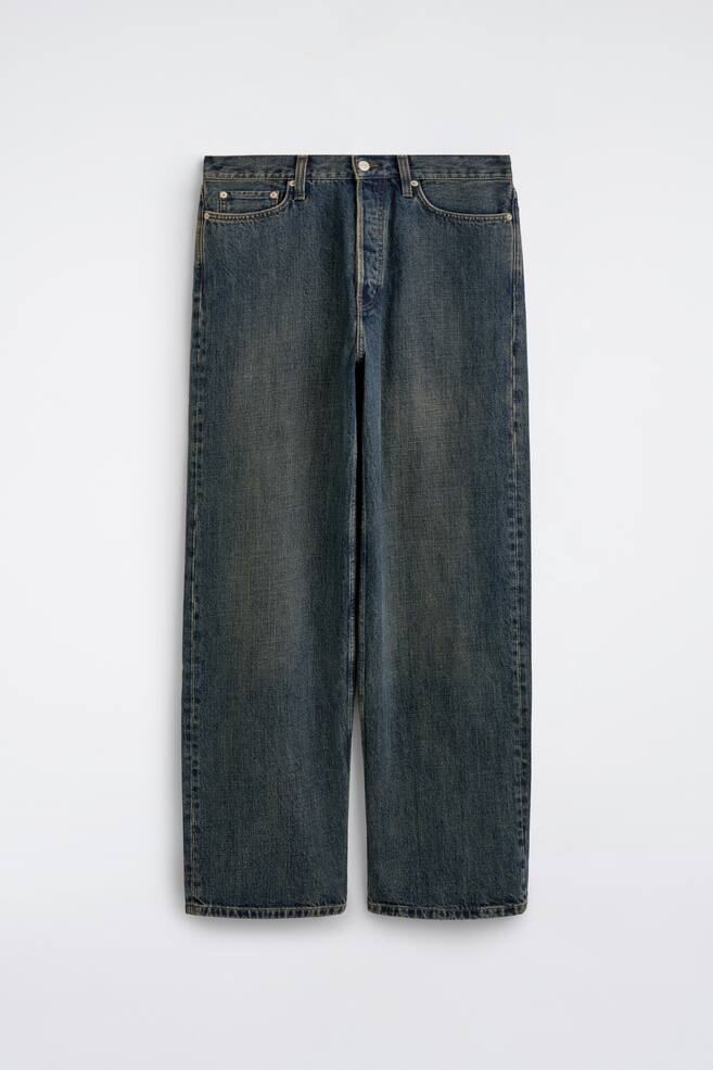 A pair of wide-leg denim jeans in a faded blue wash hangs facing front, displaying a relaxed, straight-leg silhouette with subtle vintage-style fading down the thighs. The jeans feature a classic five-pocket design, belt loops, and a button-fly closure. - 1