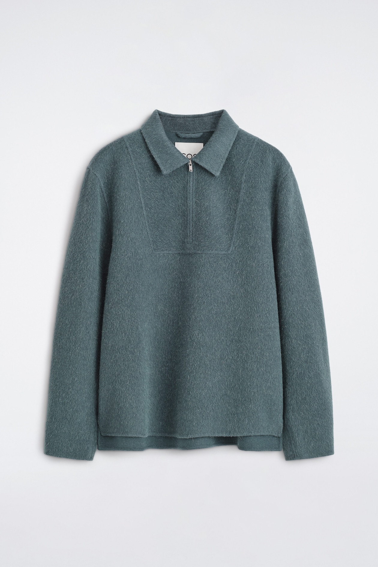 This front-facing dusty teal pullover features a textured, fuzzy finish, a spread collar, and a half-zip closure. It shows a rectangular stitched panel on the chest, long sleeves with clean-cut cuffs, and a slightly stepped hem.