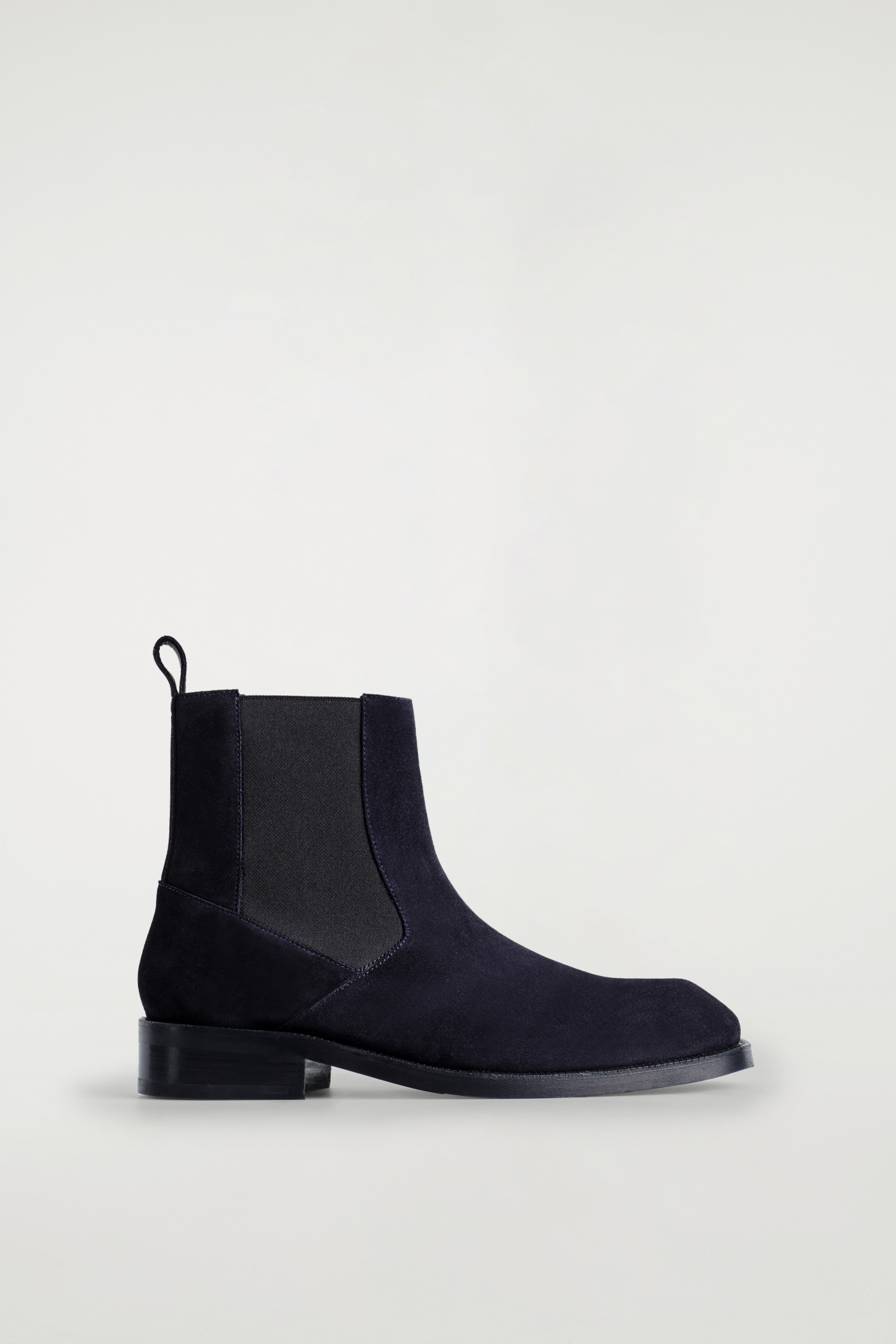 Agrandir l'image: Une botte Chelsea en cuir suédé foncé est présentée face à droite, avec un bout carré contemporain, un insert élastique sur le côté et une languette à l'arrière de la cheville.