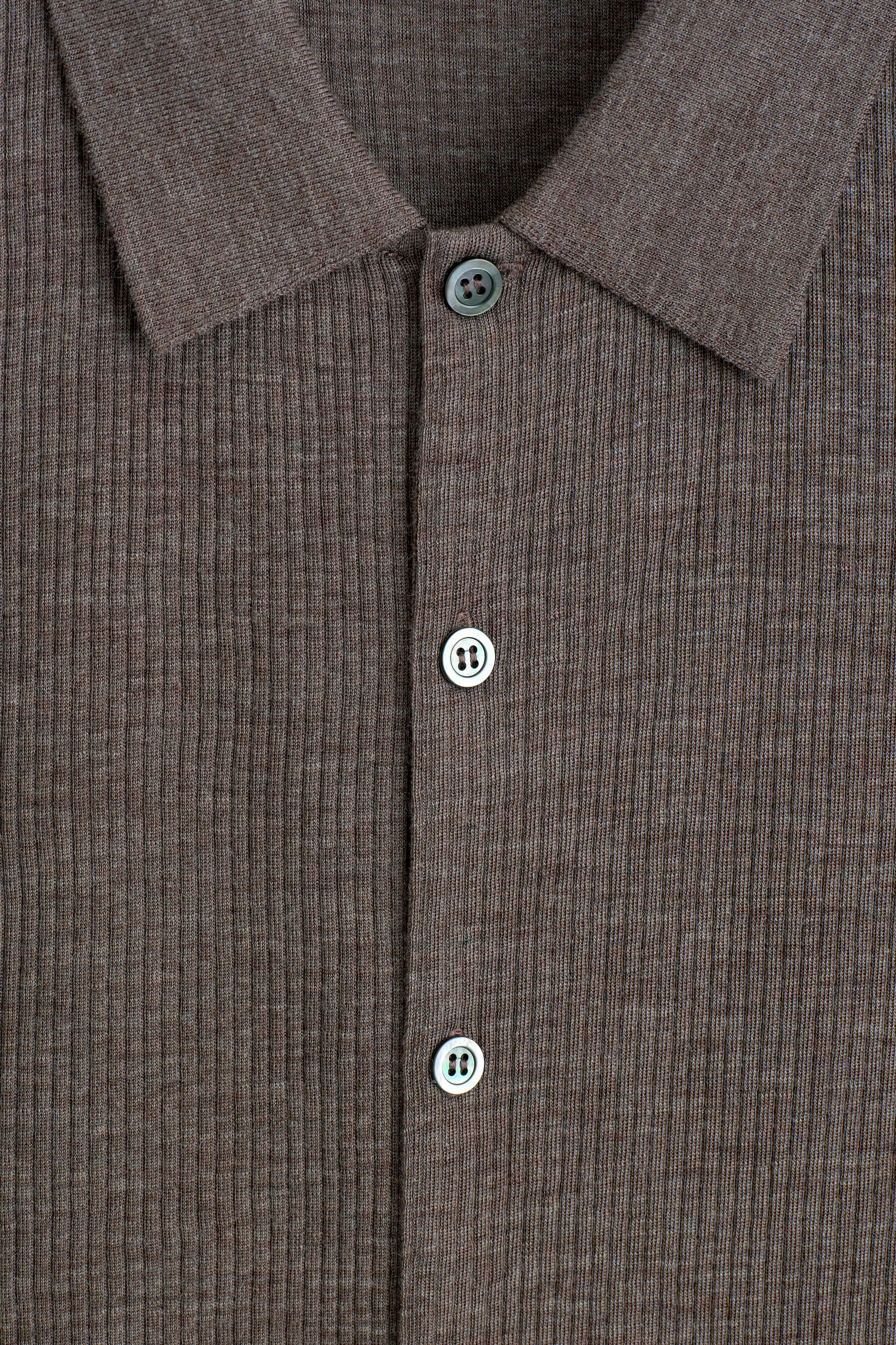 Das SLIM RIBBED WOOL SHIRT präsentiert eine Nahaufnahme der Vorderansicht seiner melierten, braunen, vertikal gerippten Strickstruktur. Das Shirt zeigt einen klassischen Kentkragen und eine vordere Knopfleiste mit drei grauen Knöpfen. Das SLIM RIBBED WOOL SHIRT präsentiert eine Nahaufnahme der Vorderansicht seiner melierten, braunen, vertikal gerippten Strickstruktur. Das Shirt zeigt einen klassischen Kentkragen und eine vordere Knopfleiste mit drei grauen Knöpfen.