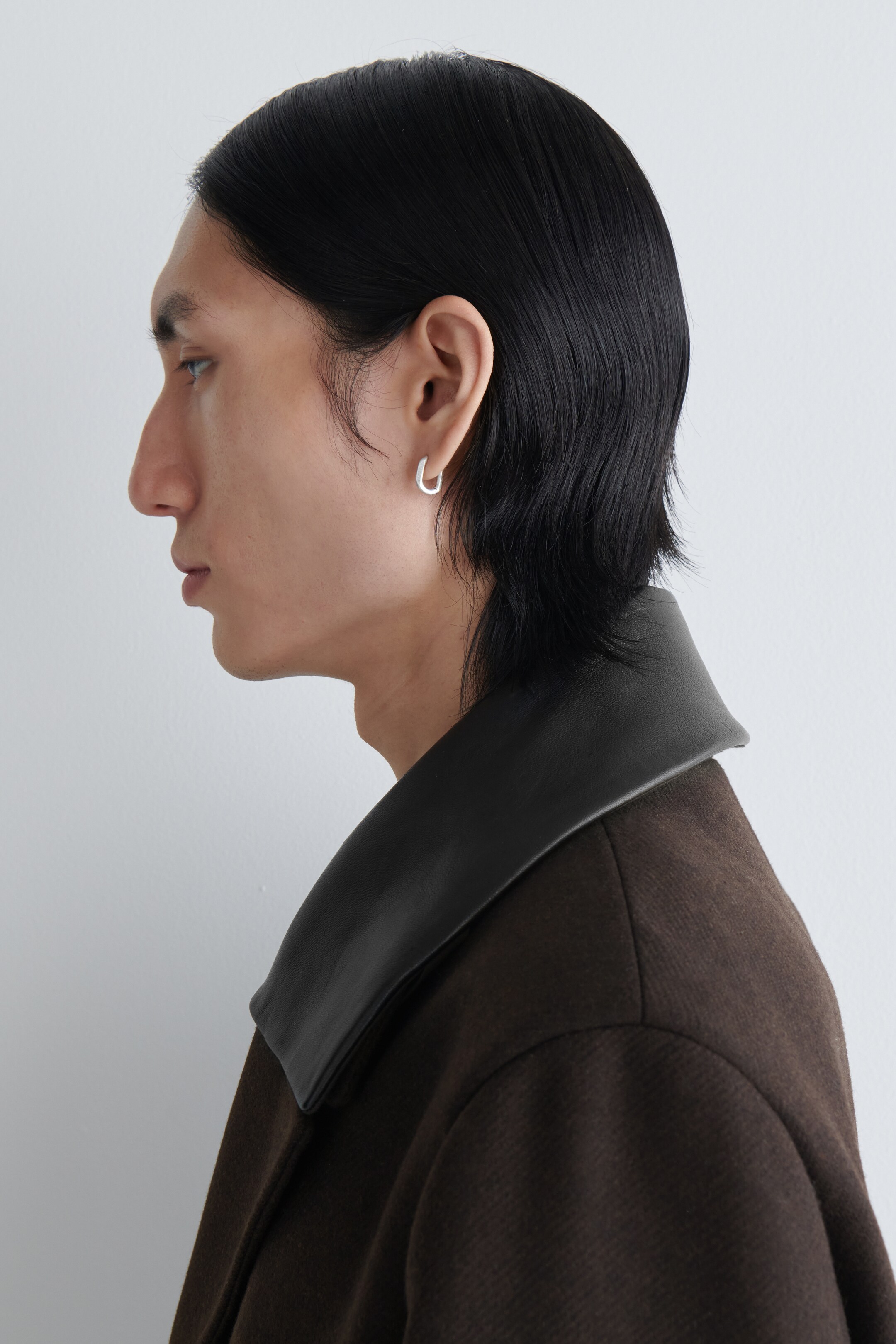 Agrandir l'image: Une boucle d'oreille en forme de U, de couleur argentée, est portée sur un lobe d'oreille, présentée en vue de profil.