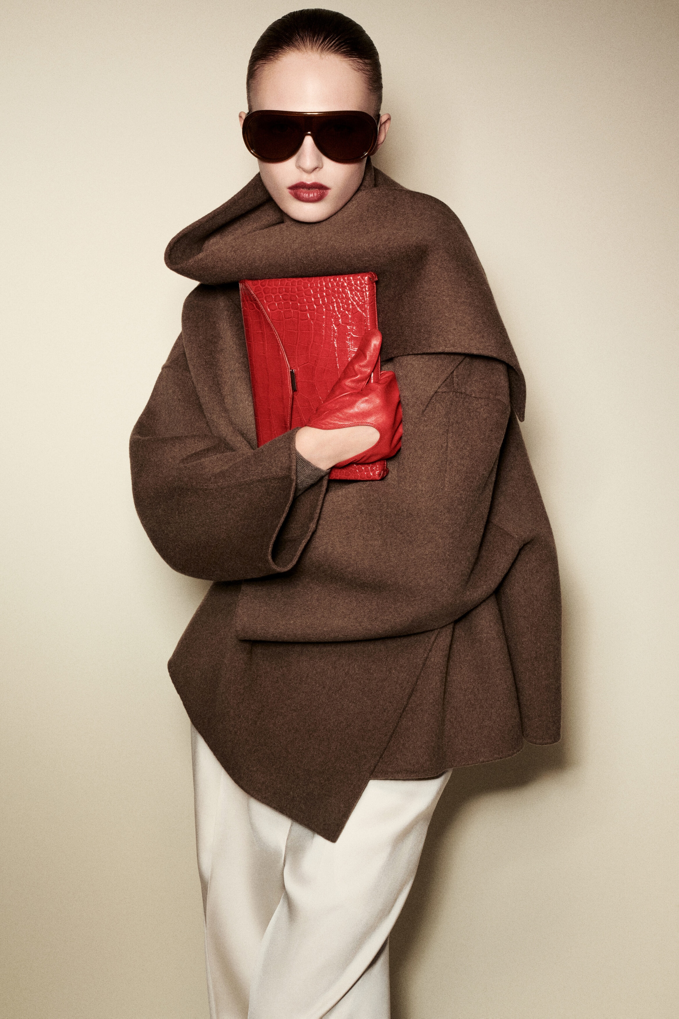 The Double-Faced Wool-Blend Scarf Jacket in brown is shown from the front, featuring an integrated draped scarf collar wrapped around the neck and wide, relaxed sleeves. A model is holding the red croc-effect leather Envelope Clasp Pouch, showcasing its textured finish and structured design against the draped wool fabric. The Double-Faced Wool-Blend Scarf Jacket in brown is shown from the front, featuring an integrated draped scarf collar wrapped around the neck and wide, relaxed sleeves. A model is holding the red croc-effect leather Envelope Clasp Pouch, showcasing its textured finish and structured design against the draped wool fabric.