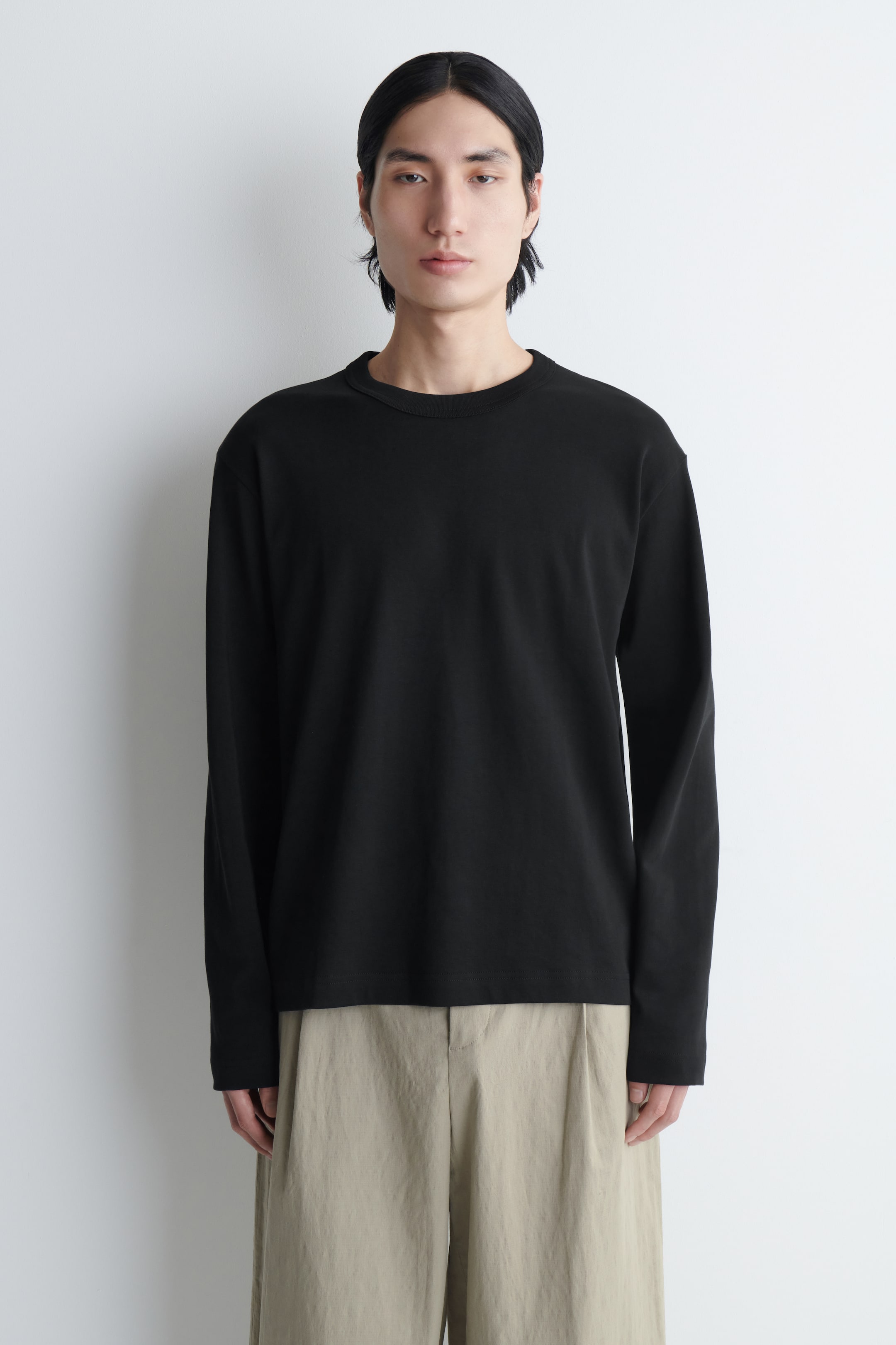 Agrandir l'image: Le modèle porte un T-shirt noir à manches longues avec un col rond. Il présente une coupe décontractée et est assorti à un pantalon de couleur claire.
