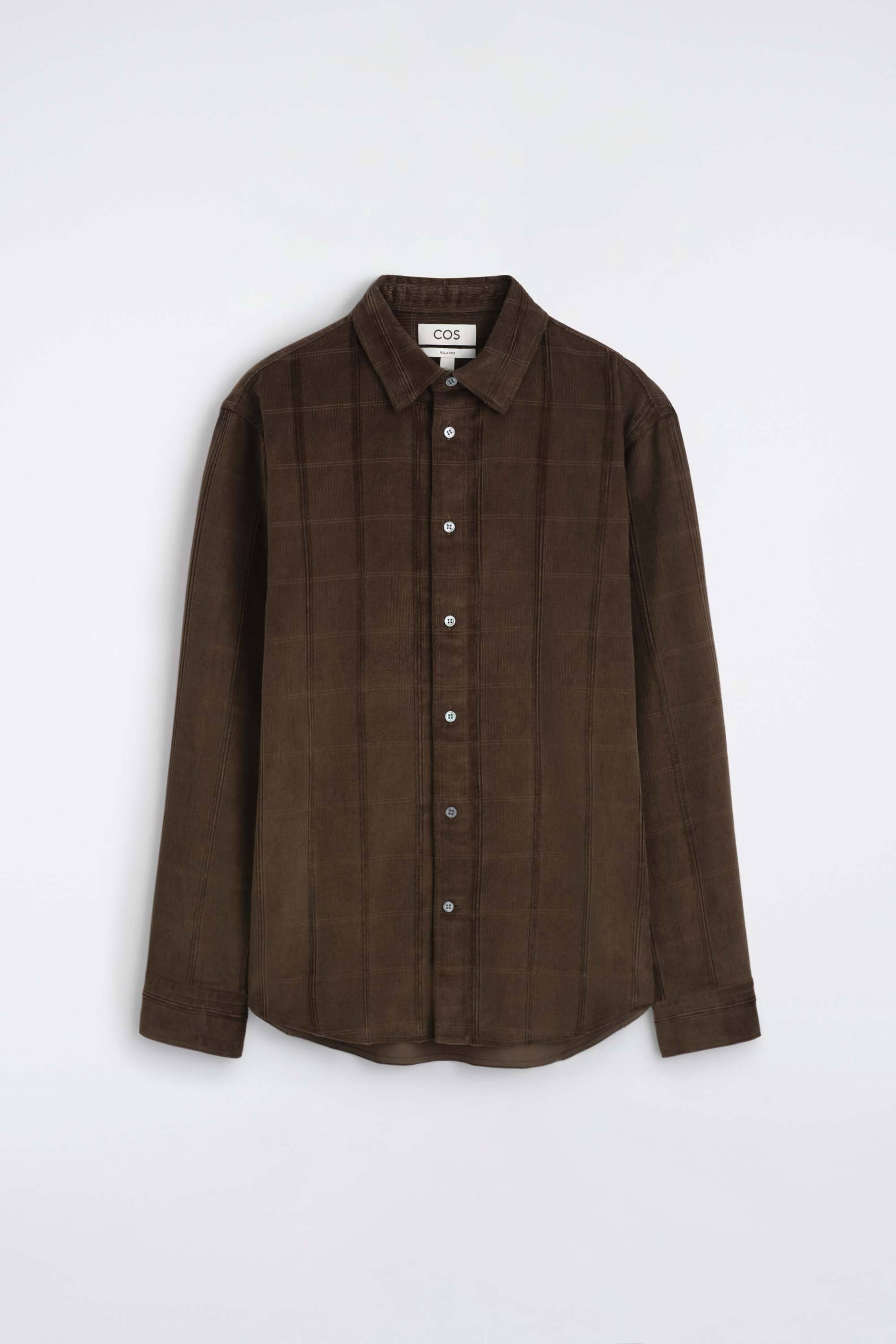 Visualizza l'immagine ingrandita: Una camicia in velluto a coste marrone scuro è mostrata frontalmente, con colletto a punta, chiusura frontale con bottoni e maniche lunghe con polsini. La camicia mette in evidenza un tessuto testurizzato con coste verticali in velluto e un delicato motivo a griglia.
