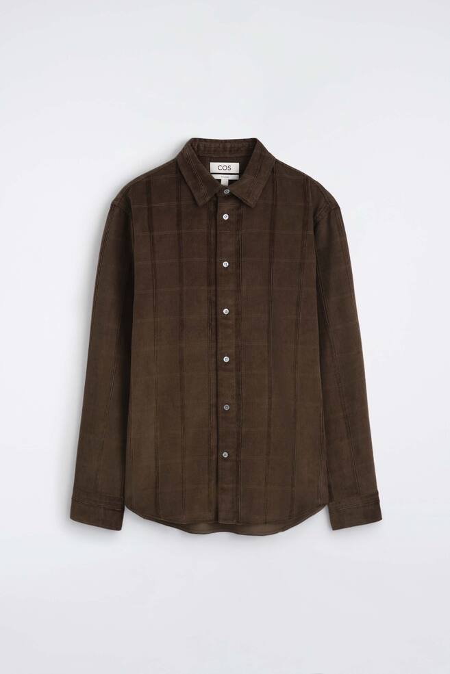 Een casual corduroy overhemd in donkerbruin wordt van voren getoond, met een puntkraag, een geknoopte knoopsluiting en lange mouwen met manchetten. Het overhemd toont een gestructureerde stof met verticale corduroyribbels en een subtiel rasterpatroon. - 1