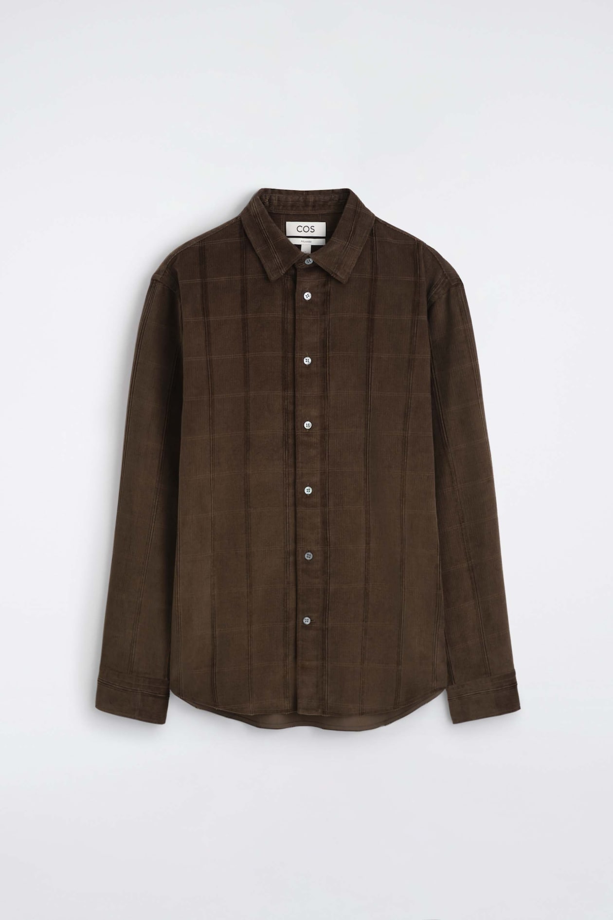 A relaxed corduroy shirt in dark brown is shown from the front, featuring a pointed collar, a buttoned front placket, and long sleeves with cuffs. The shirt is displayed in a textured fabric with vertical corduroy ribs and a subtle grid pattern.