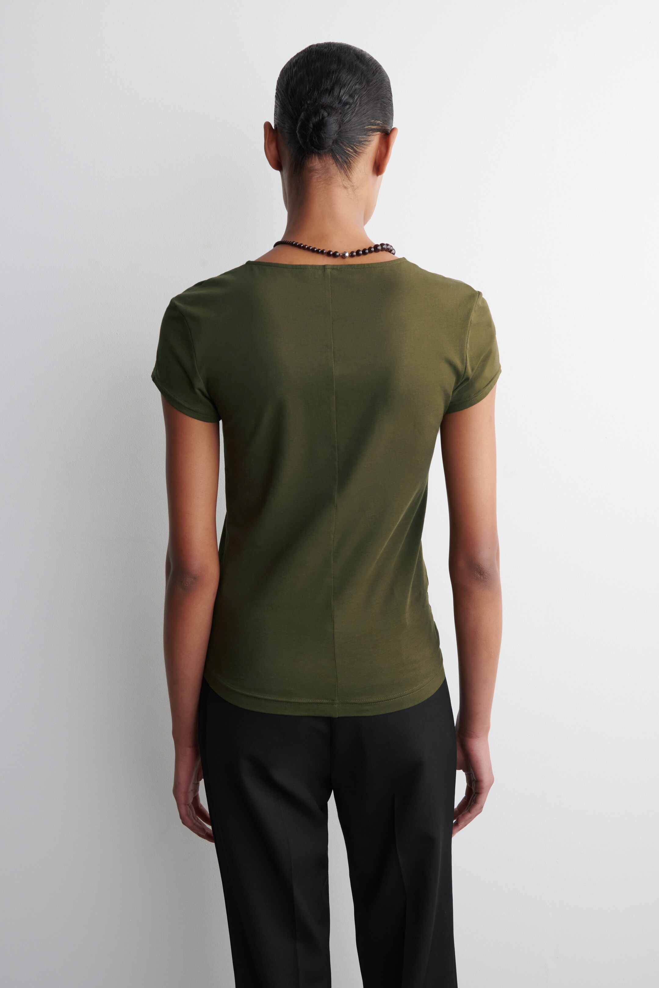 Größeres Bild anzeigen: Ein olivgrünes T-Shirt wird von hinten getragen und zeigt seine figurbetonte Silhouette. Es hat kurze Ärmel und eine markante vertikale Naht, die in der Mitte des Rückens verläuft.