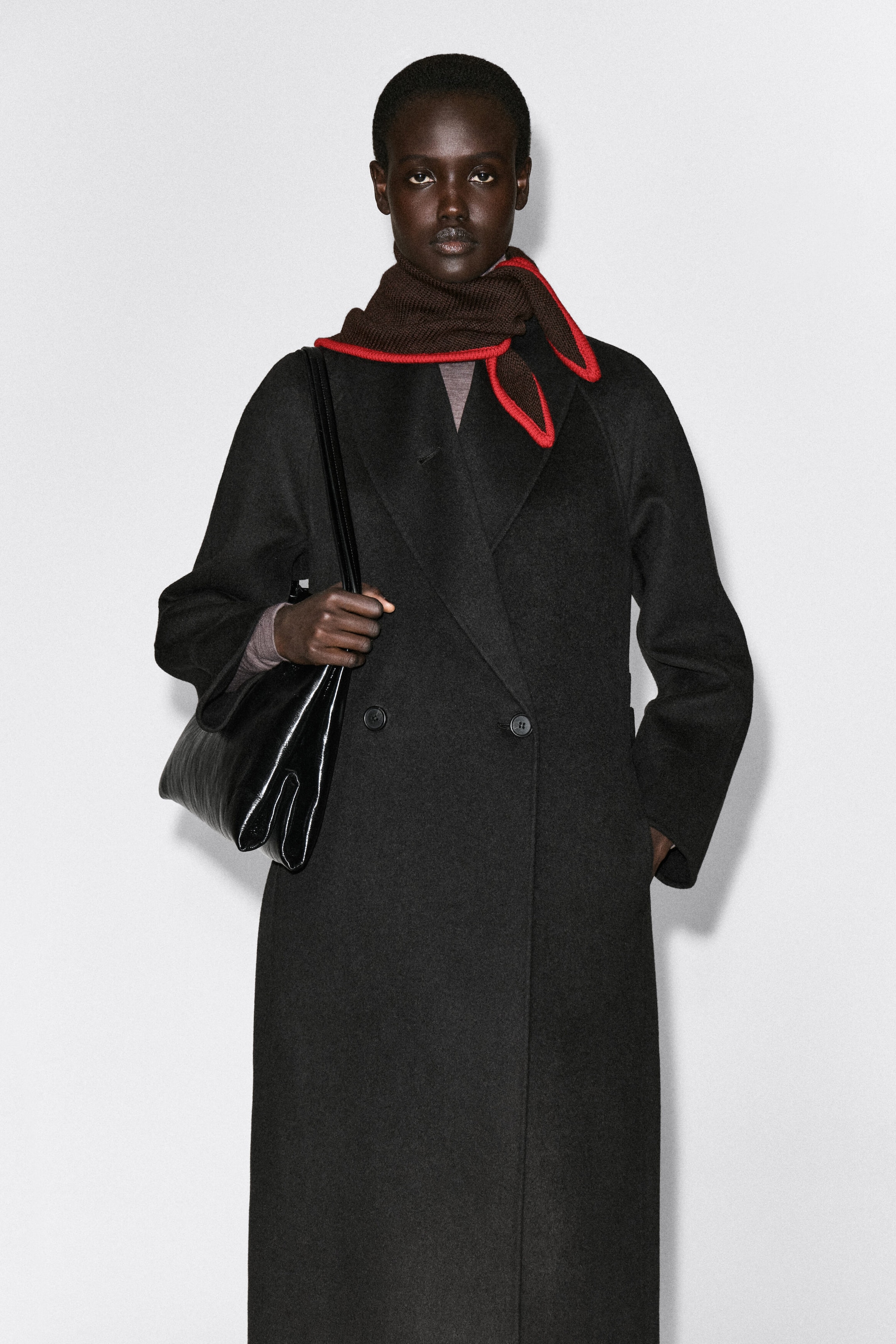 Le foulard triangle en laine mérinos marron foncé à extrémités contrastantes est porté enroulé autour du cou, associé à un manteau croisé sombre sur un mannequin de face. Le foulard présente une bordure contrastante rouge vif le long de ses bords, avec les pointes tombant sur l’épaule. Le foulard triangle en laine mérinos marron foncé à extrémités contrastantes est porté enroulé autour du cou, associé à un manteau croisé sombre sur un mannequin de face. Le foulard présente une bordure contrastante rouge vif le long de ses bords, avec les pointes tombant sur l’épaule.