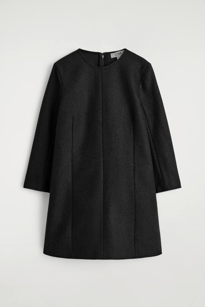 Une mini-robe noire est présentée de face, avec une encolure arrondie, des manches longues et un tissu texturé mat. Des coutures verticales visibles apportent une structure à sa silhouette. - 1