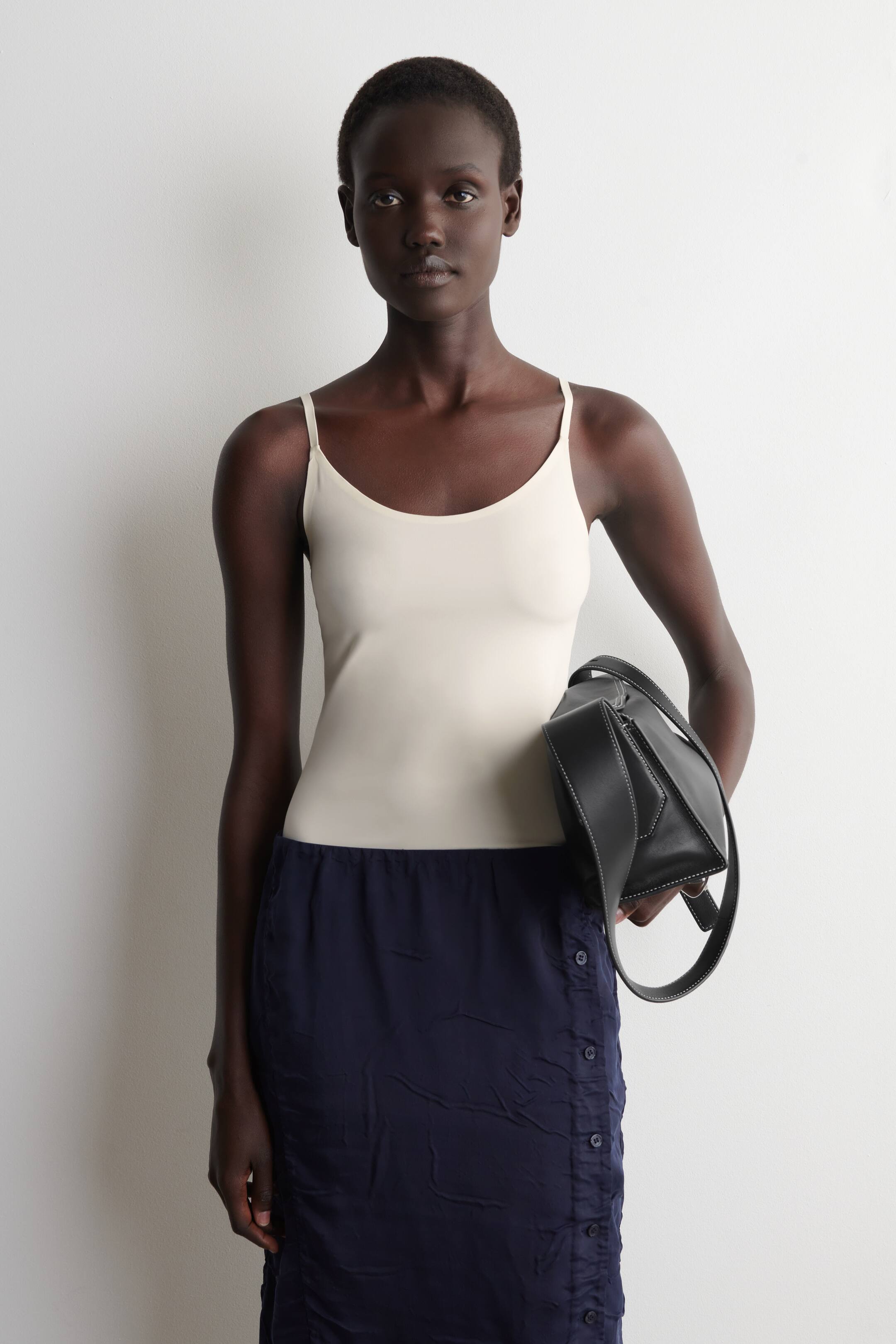 Agrandir l'image: Le débardeur blanc cassé est présenté de face, avec un décolleté arrondi et de fines bretelles spaghetti. Il épouse étroitement le corps, mettant en valeur un design lisse et ajusté.