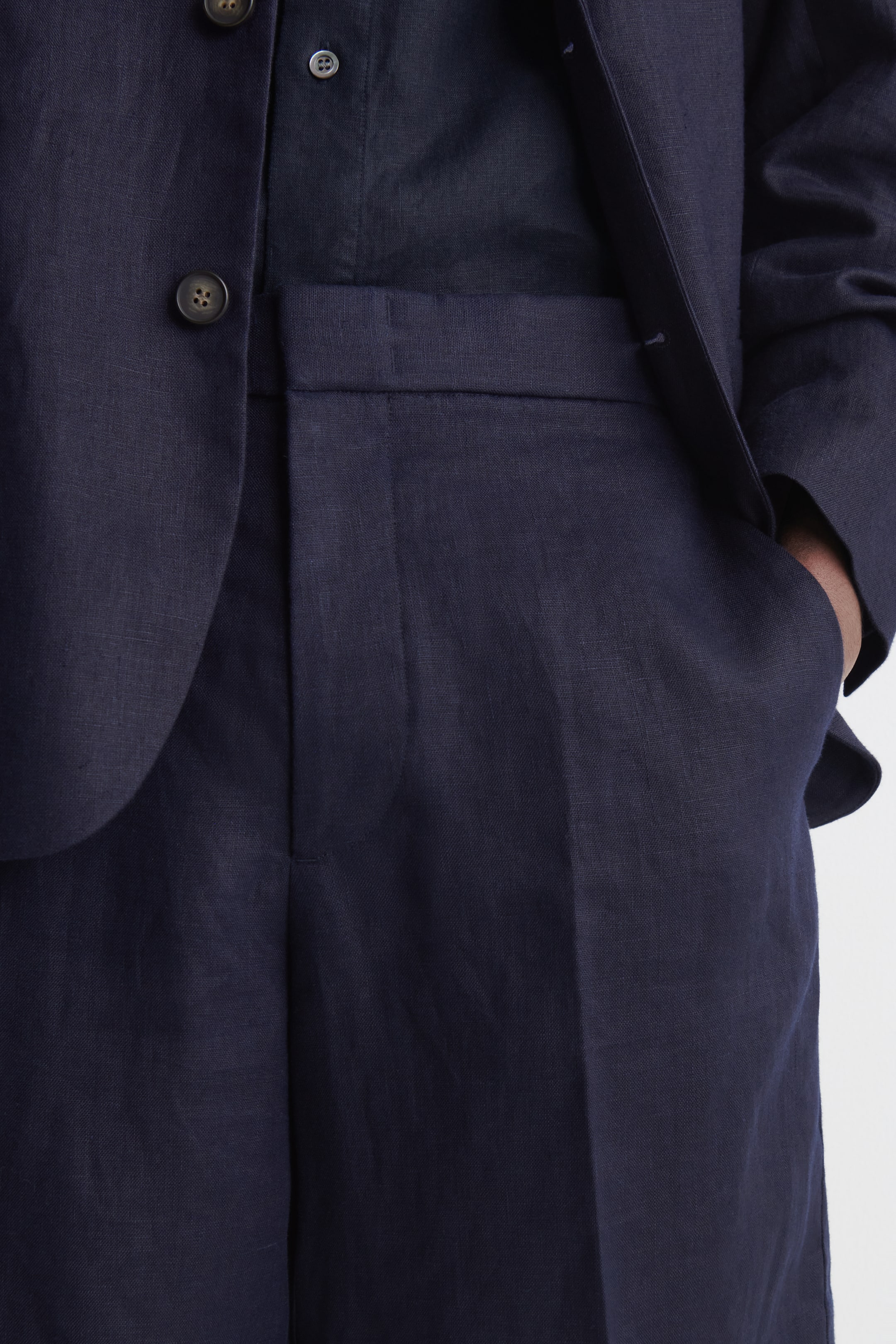 Visualizza immagine più grande: Una giacca da abito in lino blu navy presenta una chiusura con bottoni scuri ed è indossata sopra una camicia scura. Viene indossato anche un pantalone abbinato a taglio dritto, con una mano appoggiata nella tasca laterale destra.