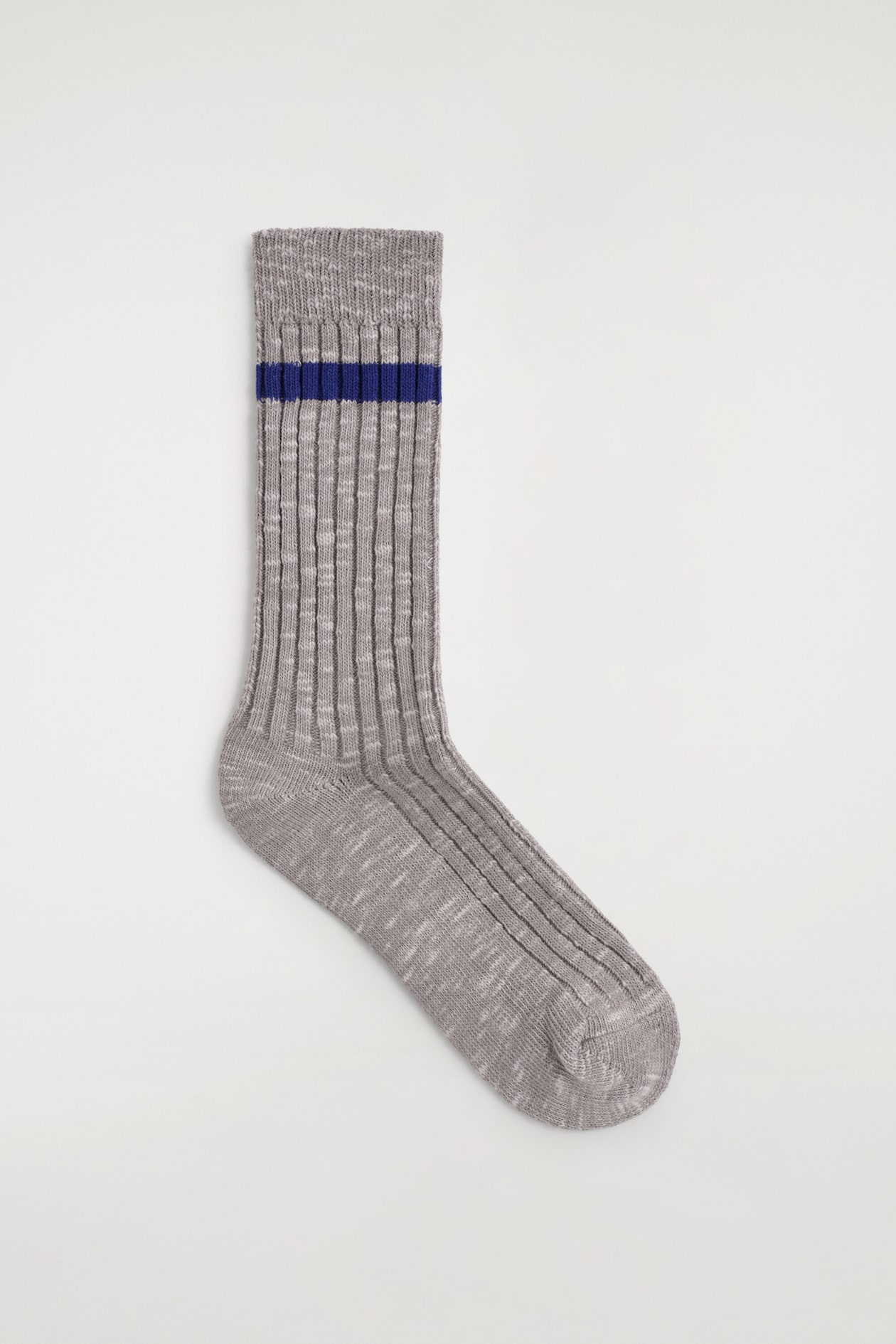 Une chaussette côtelée chinée gris est posée à plat, mettant en valeur sa texture côtelée verticale et une seule rayure horizontale bleu foncé près du bord-côte supérieur. La chaussette est présentée de biais, soulignant la forme du talon, de la semelle et de la pointe.