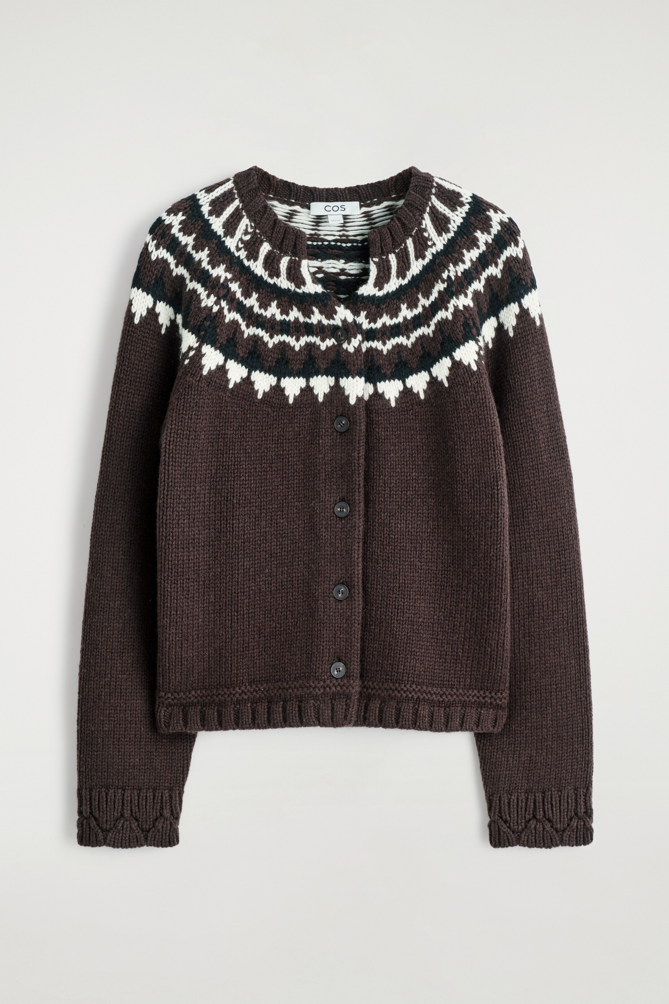 Visualizza immagine più grande: Un cardigan marrone scuro è presentato FRONT, caratterizzato da un motivo fair isle che attraversa il petto e le spalle con motivi geometrici bianchi e verde scuro. È progettato con uno scollo rotondo, una chiusura frontale con cinque bottoni scuri e bordi a coste sullo scollo, i polsini e l'orlo.