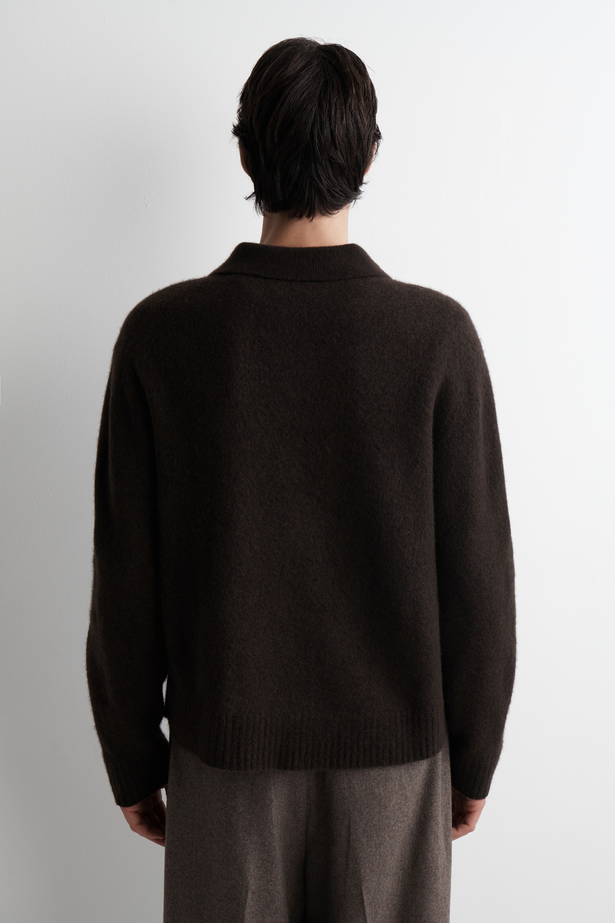 Agrandir l'image: Le DOS d'un polo tricoté brun foncé est exposé, montrant une coupe décontractée et une texture de surface brossée. Il présente un ourlet côtelé.