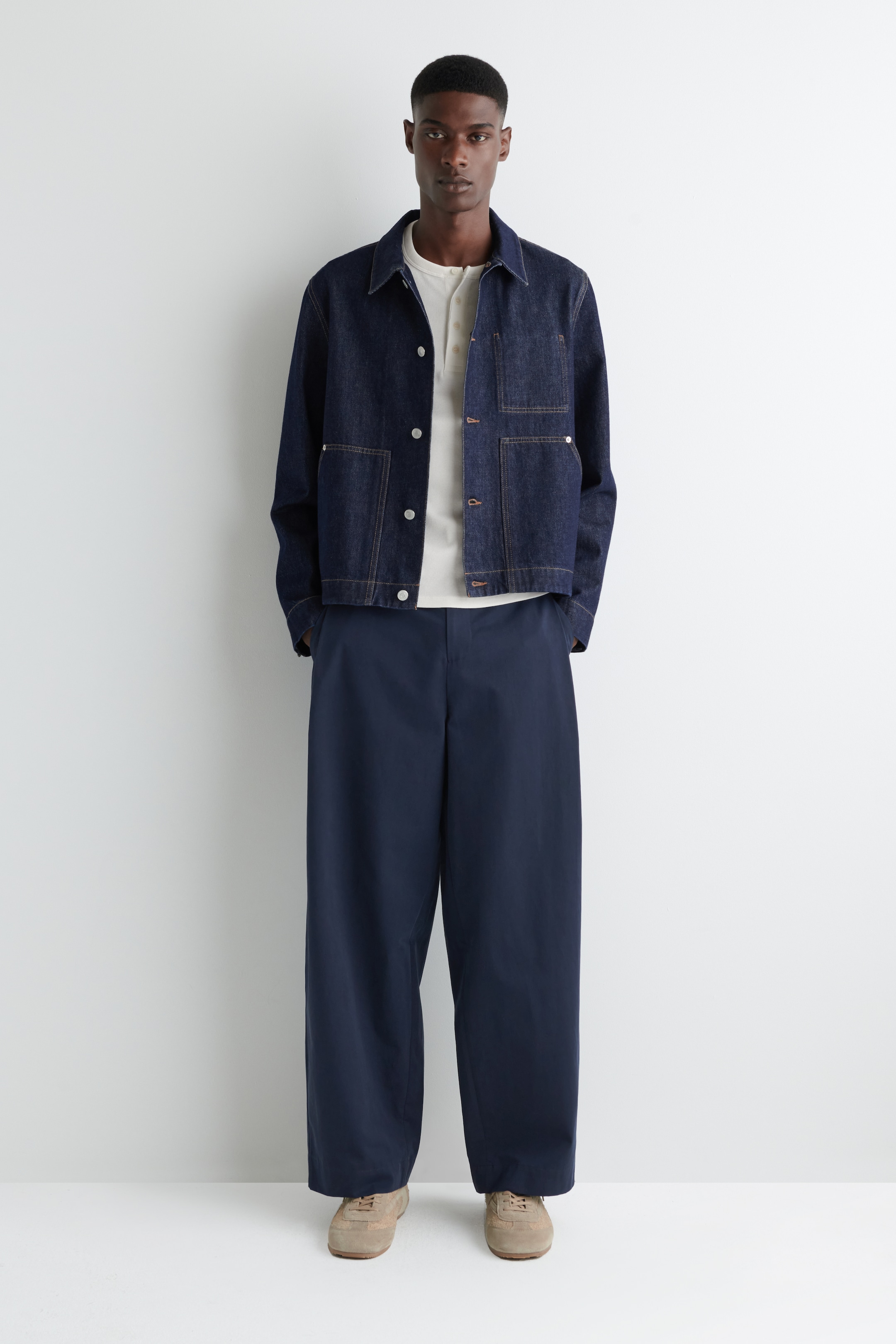 View larger image: A dark blue denim jacket is being presented from the front, featuring a pointed collar, a button-up front with light buttons, and four patch pockets with contrasting stitching. It is being worn over a light-colored henley shirt.