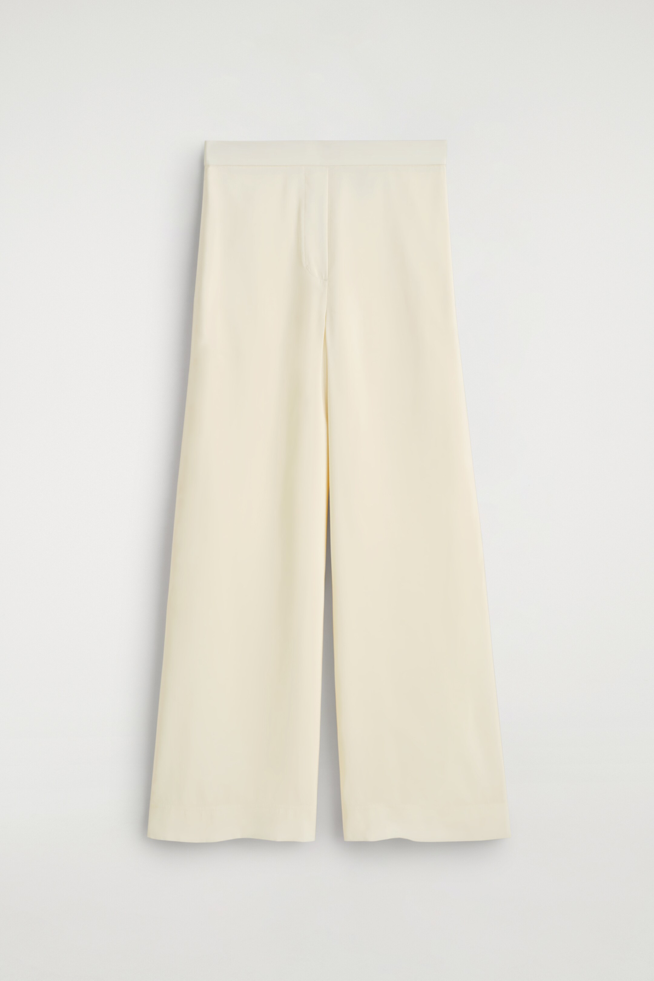 Ingrandisci l'immagine: Pantaloni a gamba larga color crema sono rivolti in avanti, con una cintura piatta e un leggero lucentezza sul tessuto. Una piega distinta corre lungo il centro anteriore di ciascuna gamba.