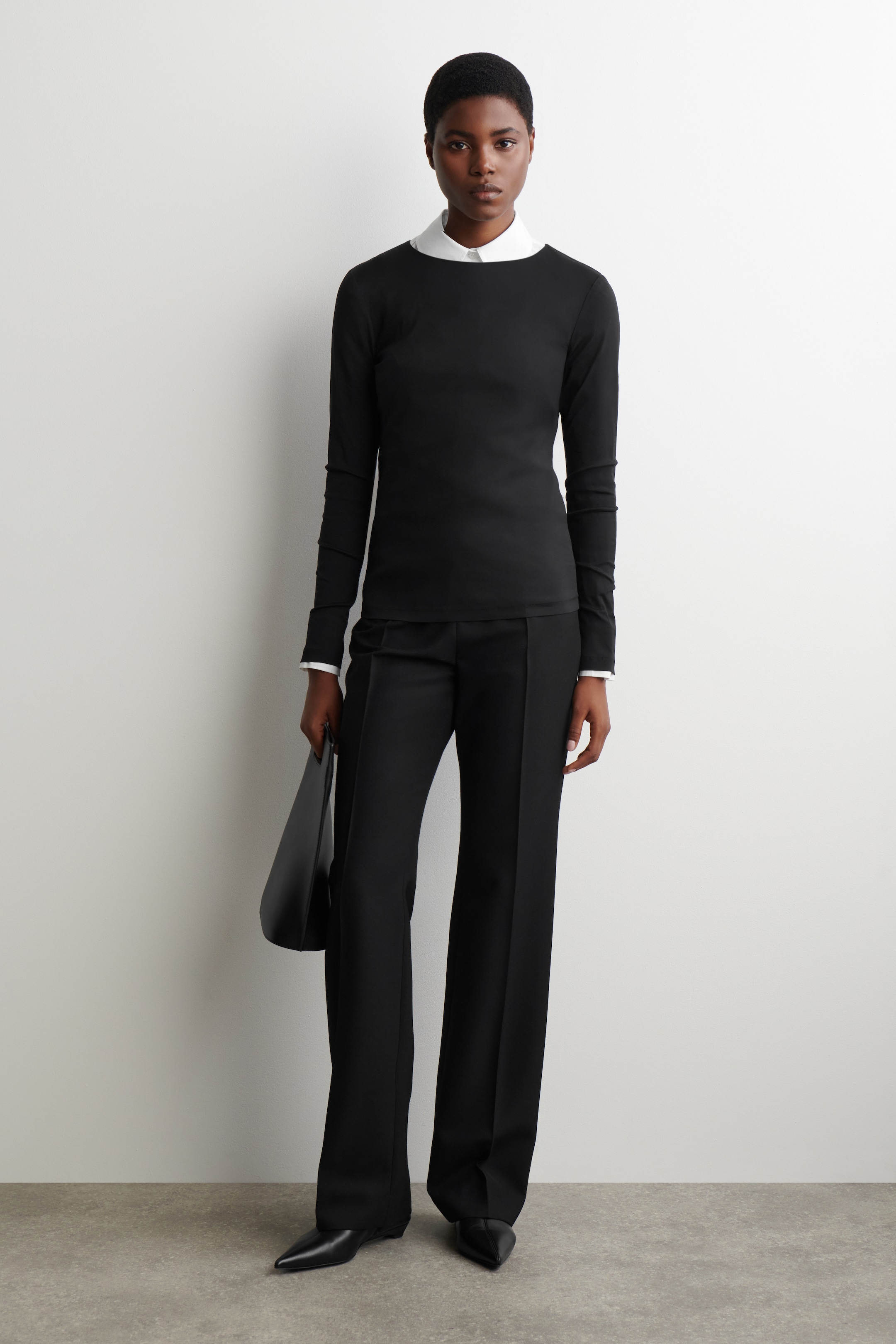 View larger image: A black slim-fit long-sleeved top with a rounded neckline is being worn by the model. A white collared shirt is layered underneath, with its collar and cuffs visible.