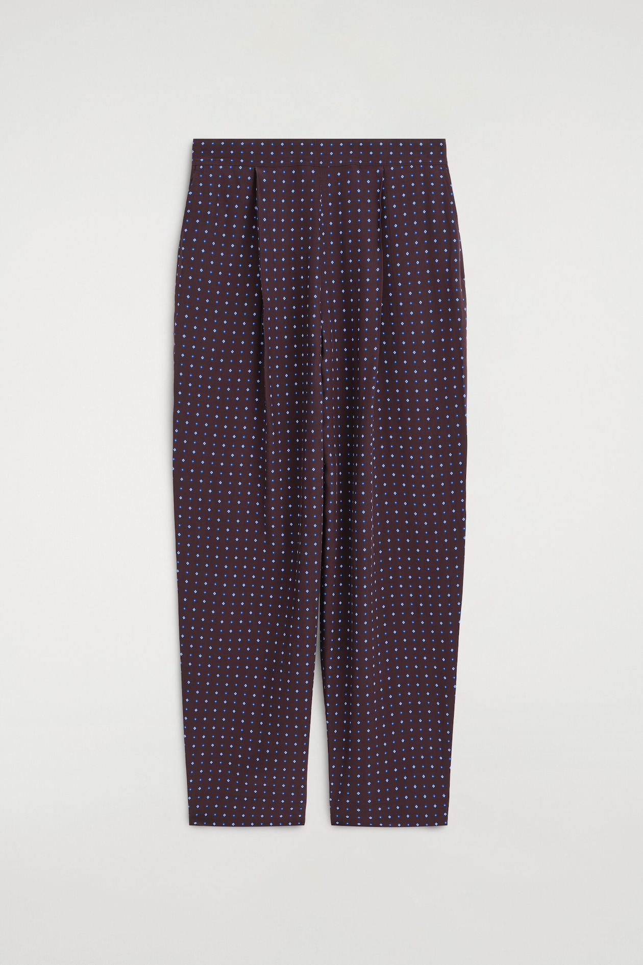 Ce pantalon droit à imprimé losanges est présenté de face, avec un tissu marron foncé orné d’un motif répétitif de petits losanges bleus. Le pantalon met en valeur une taille haute, avec des plis sur le devant et une silhouette droite.