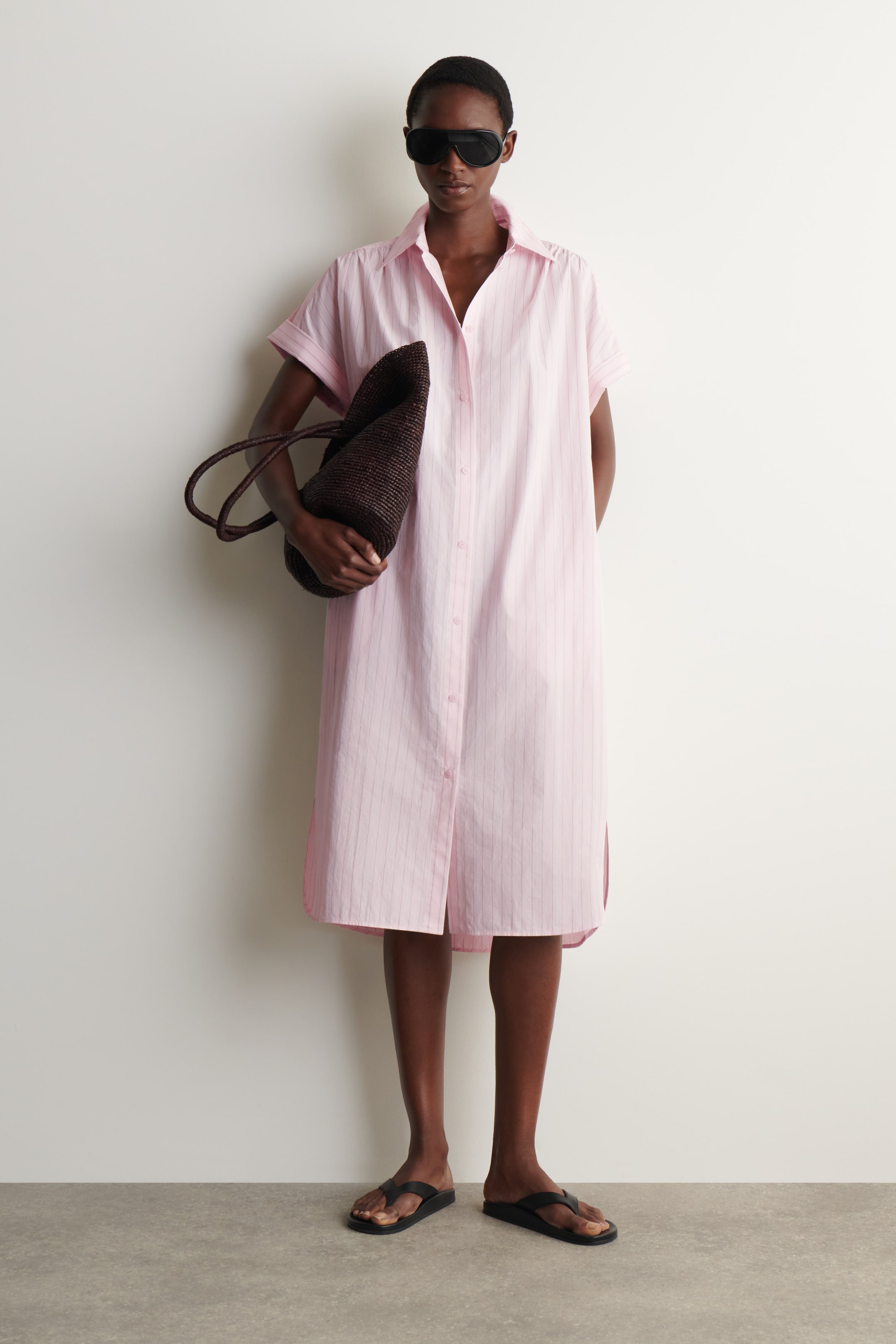 Ver imagem maior: Um vestido-camisa às riscas cor-de-rosa apresenta uma gola pontiaguda, mangas curtas com punhos e uma carcela de botões. É cortado num silhueta solta e reta com aberturas laterais, estendendo-se até um pouco abaixo do joelho.