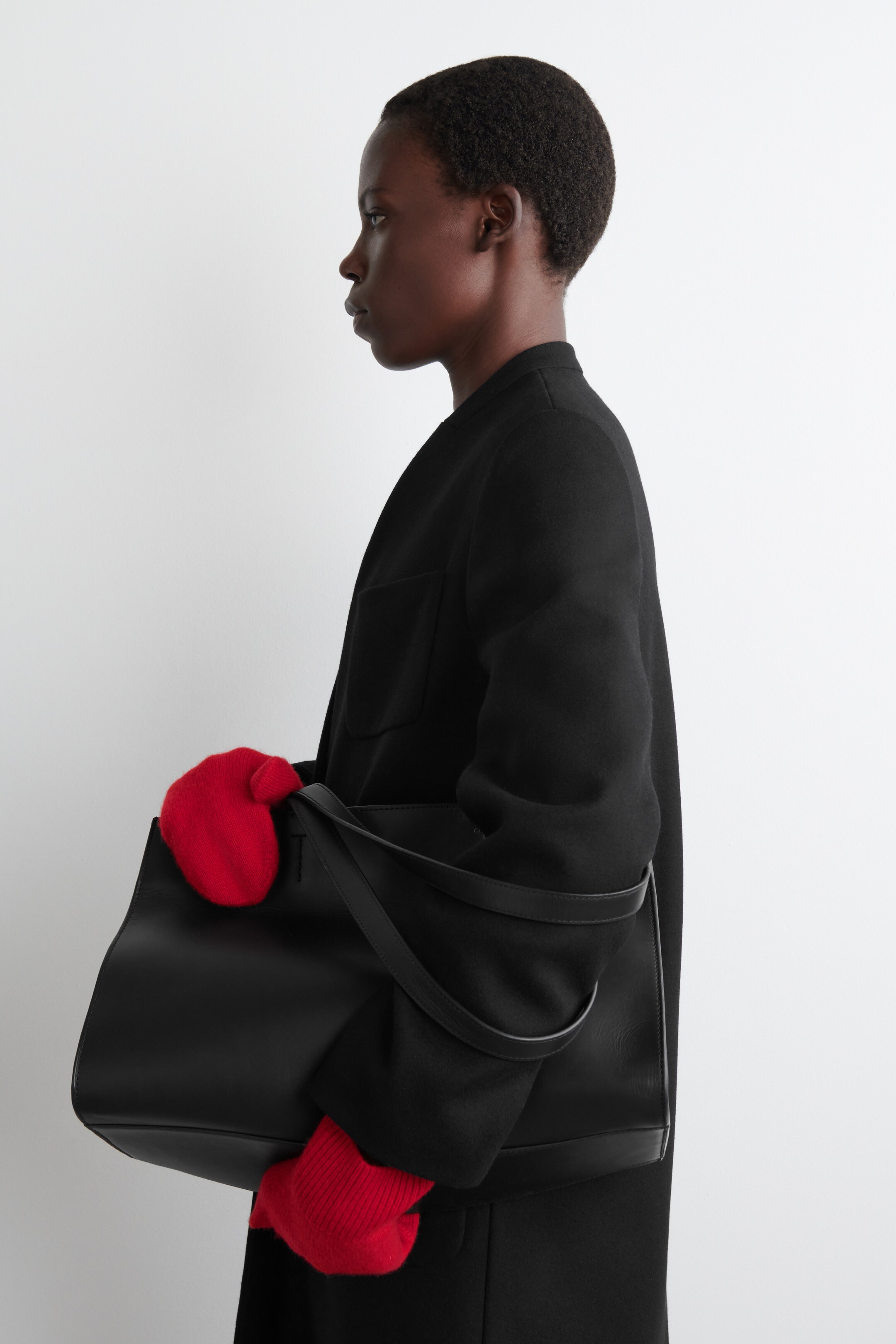 View larger image: Red knitted mittens, featuring chunky ribbed cuffs, are being worn while holding a black bag, and are shown from a left perspective.